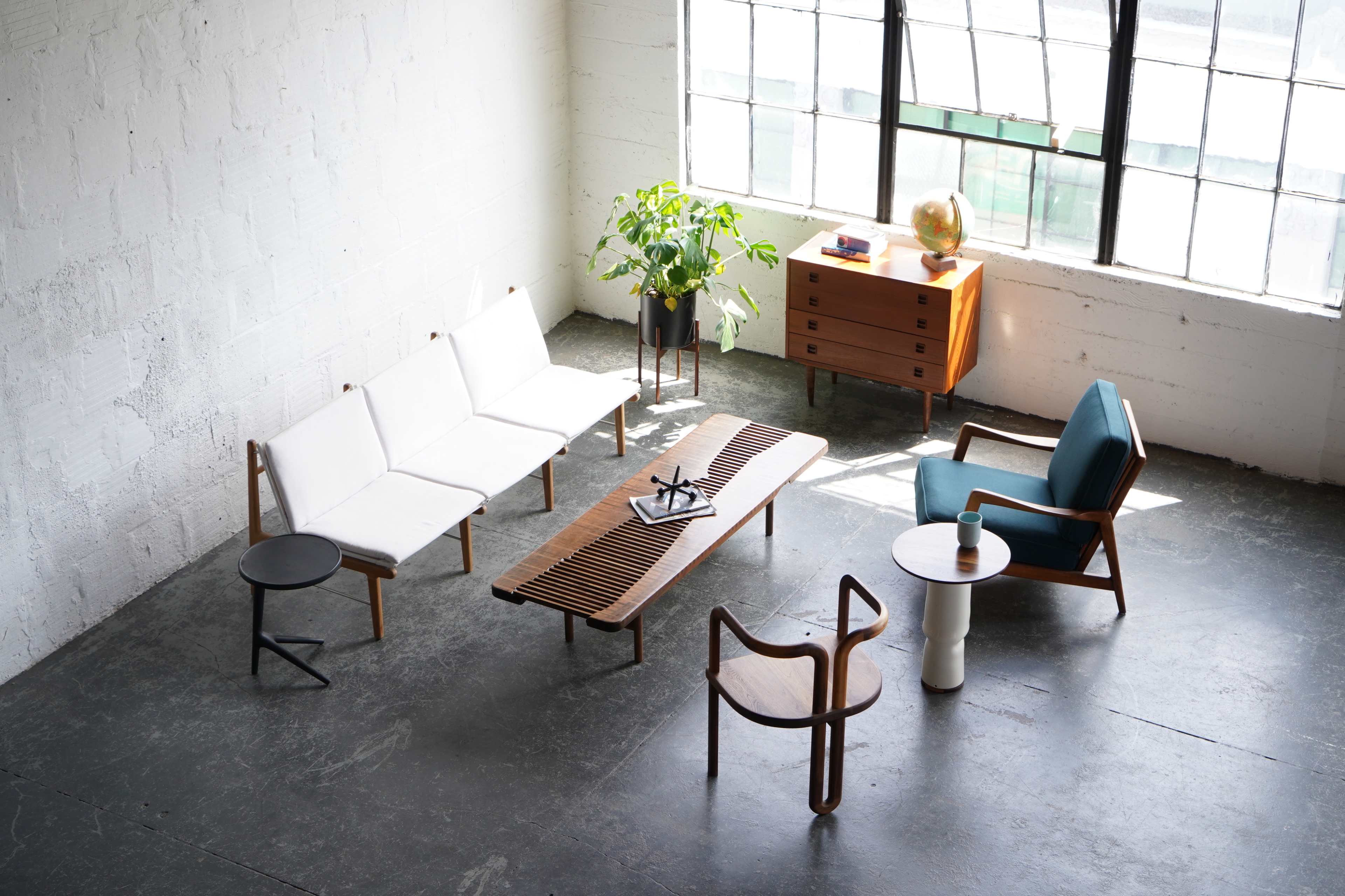 The scene features a modern living room with two sofas, a wooden coffee table, a small side table, a plant, a globe, and a storage cabinet arranged around a large window.