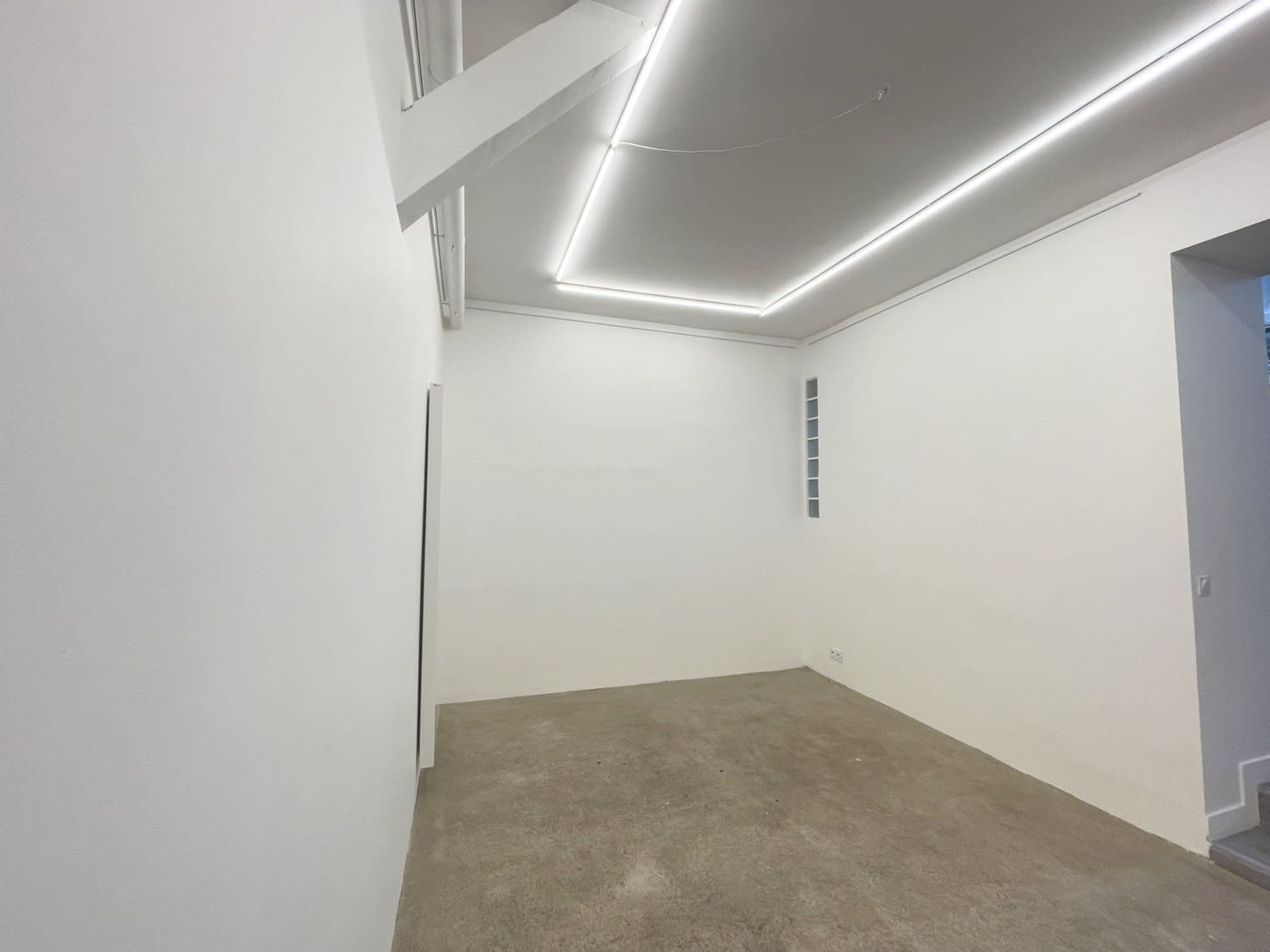 An empty, white-walled room with a concrete floor and overhead LED lighting.