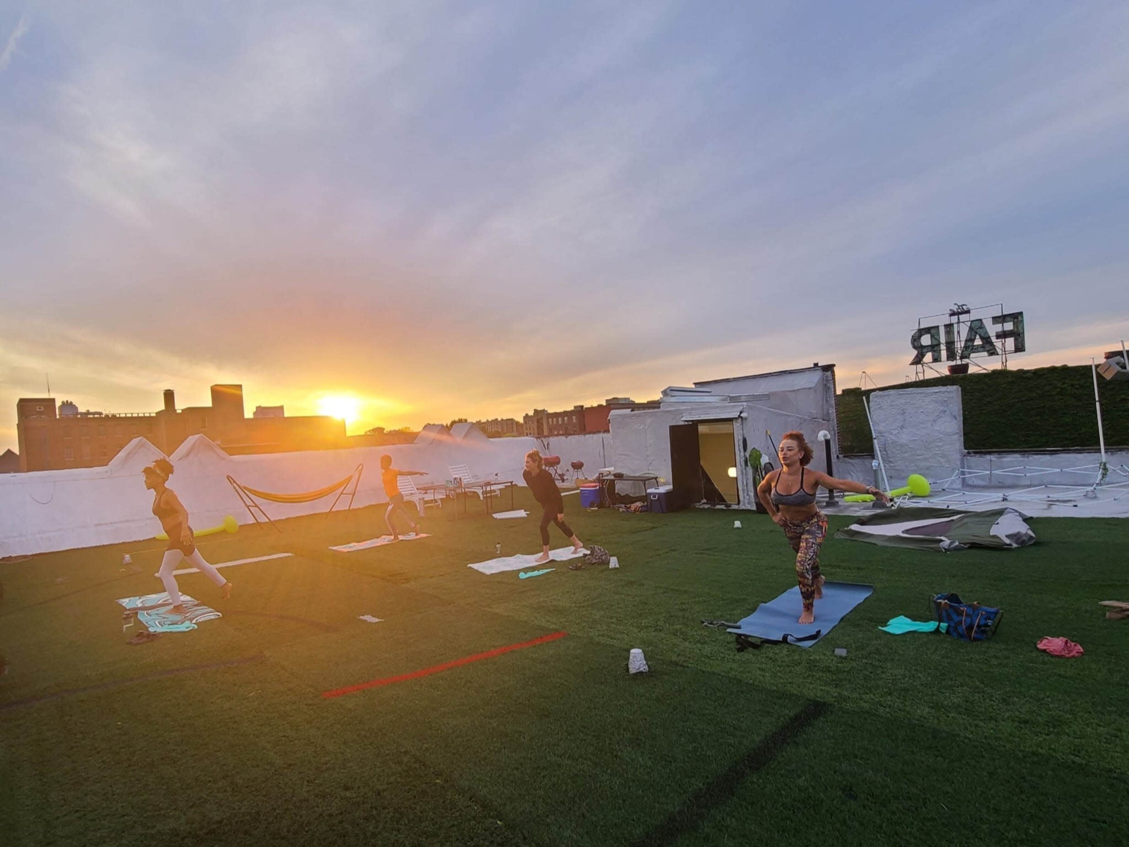 A group of people is exercising on yoga mats on a rooftop during sunset.