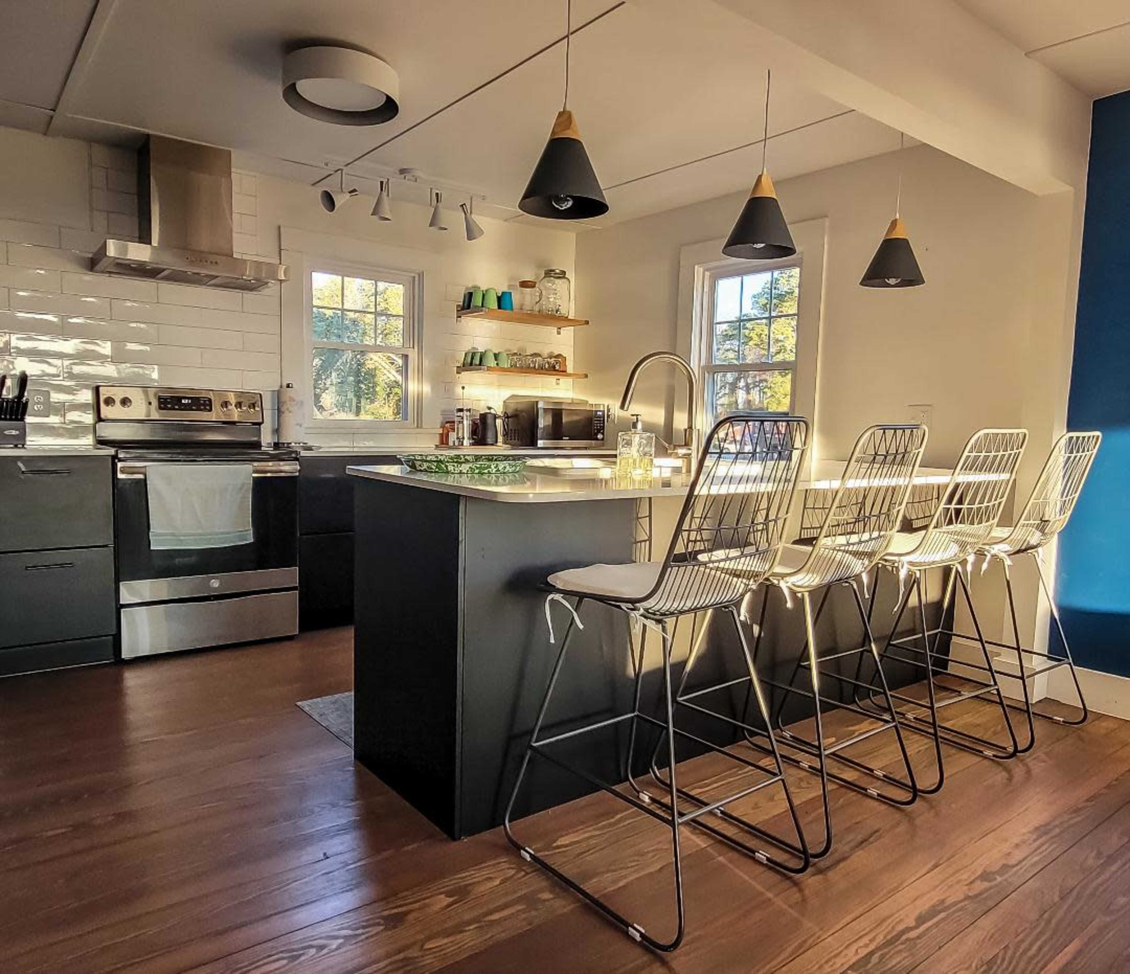 A modern kitchen with a central island, four wire-frame barstools, and pendant lighting.