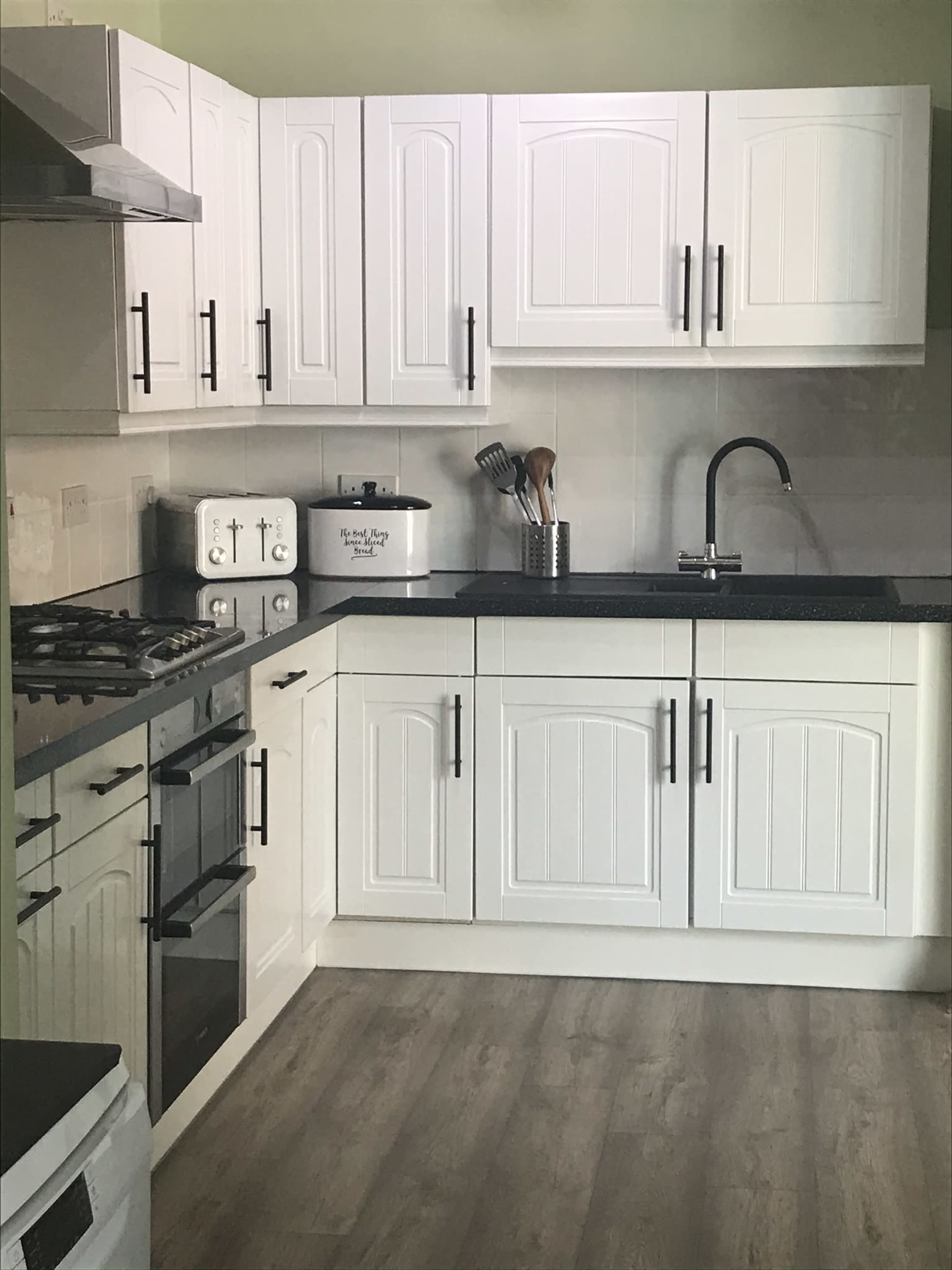 A modern kitchen with white cabinetry, a black countertop, and stainless steel appliances.