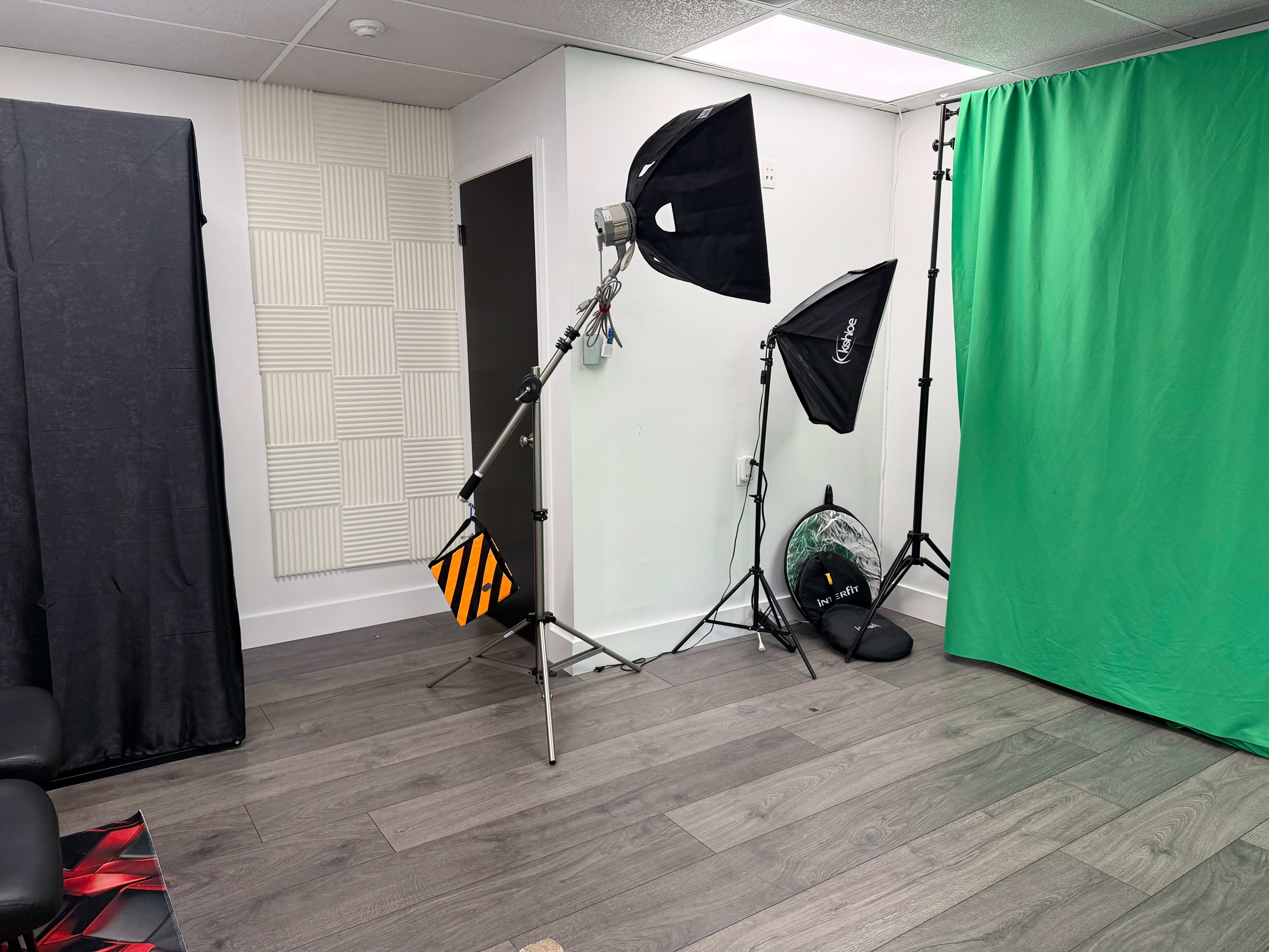 The image shows a room set up for video production, featuring a green screen, softbox lighting, and soundproof panels on one wall.