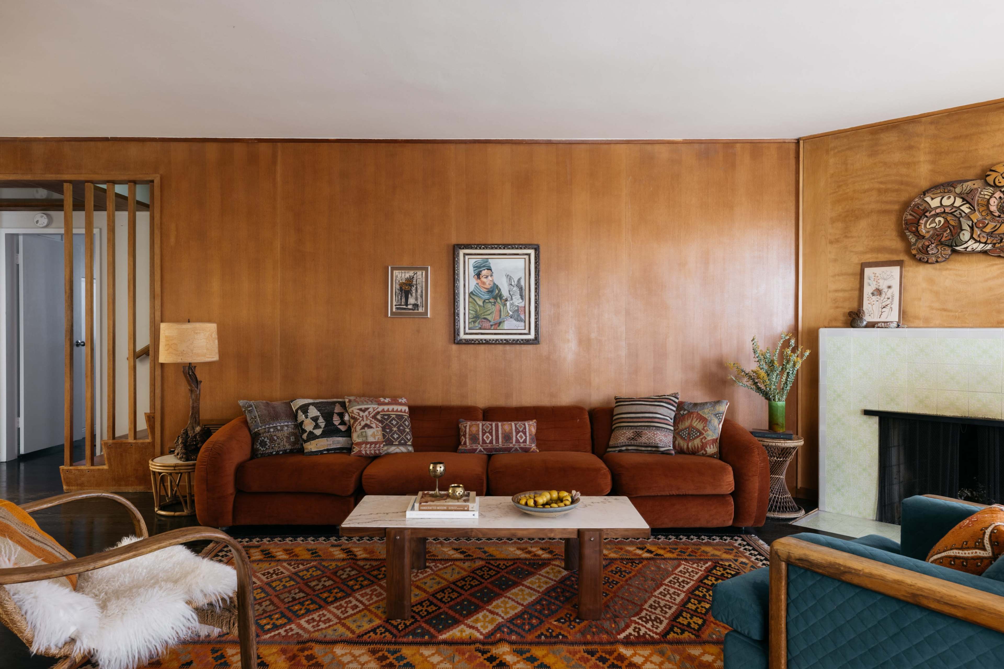 A living room with a brown sofa, a patterned rug, and a wooden accent wall featuring artwork and decorative items.