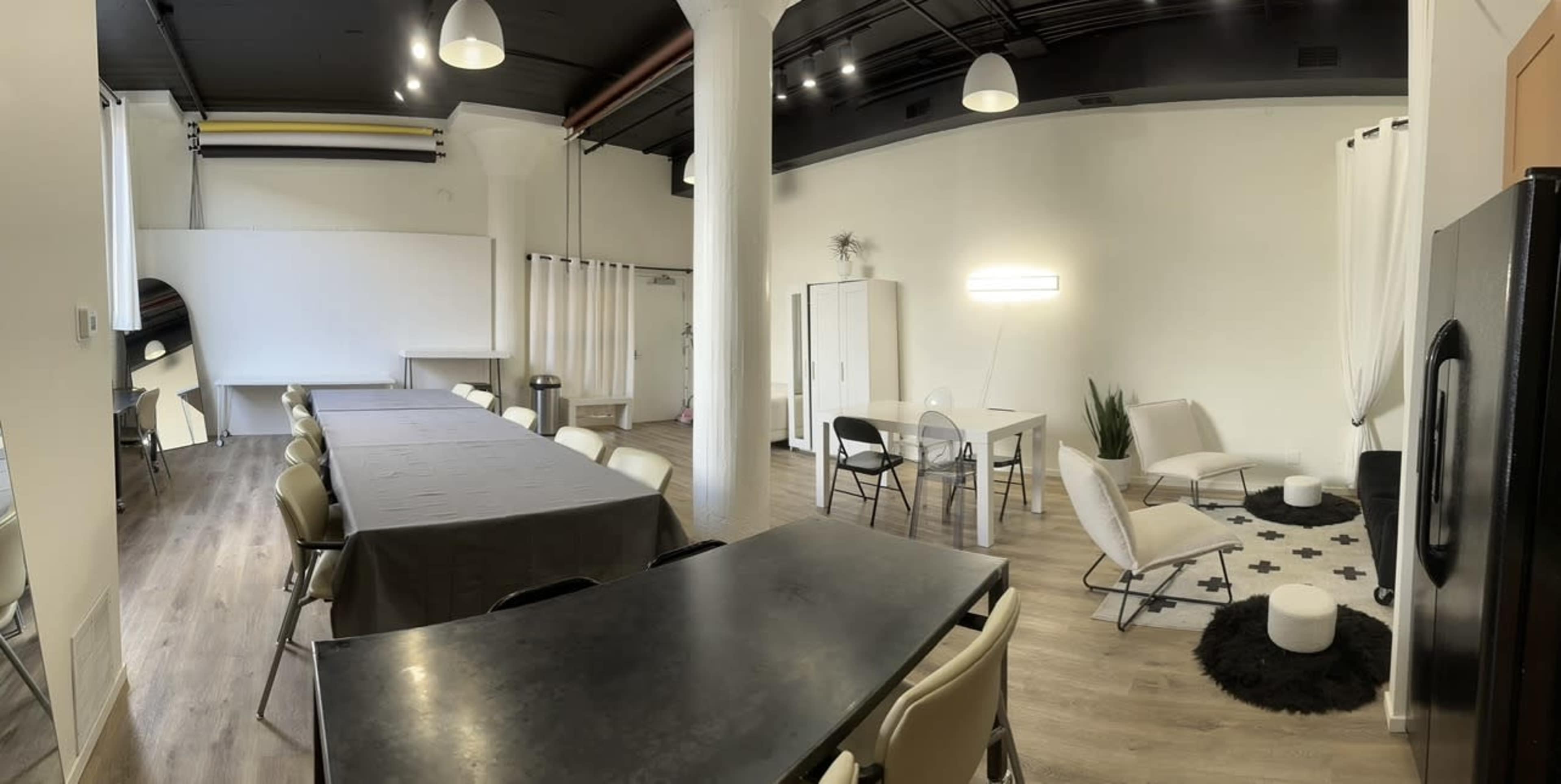 The image shows a spacious, well-lit room with a long table and chairs on one side and a seating area with a sofa and small tables on the other.