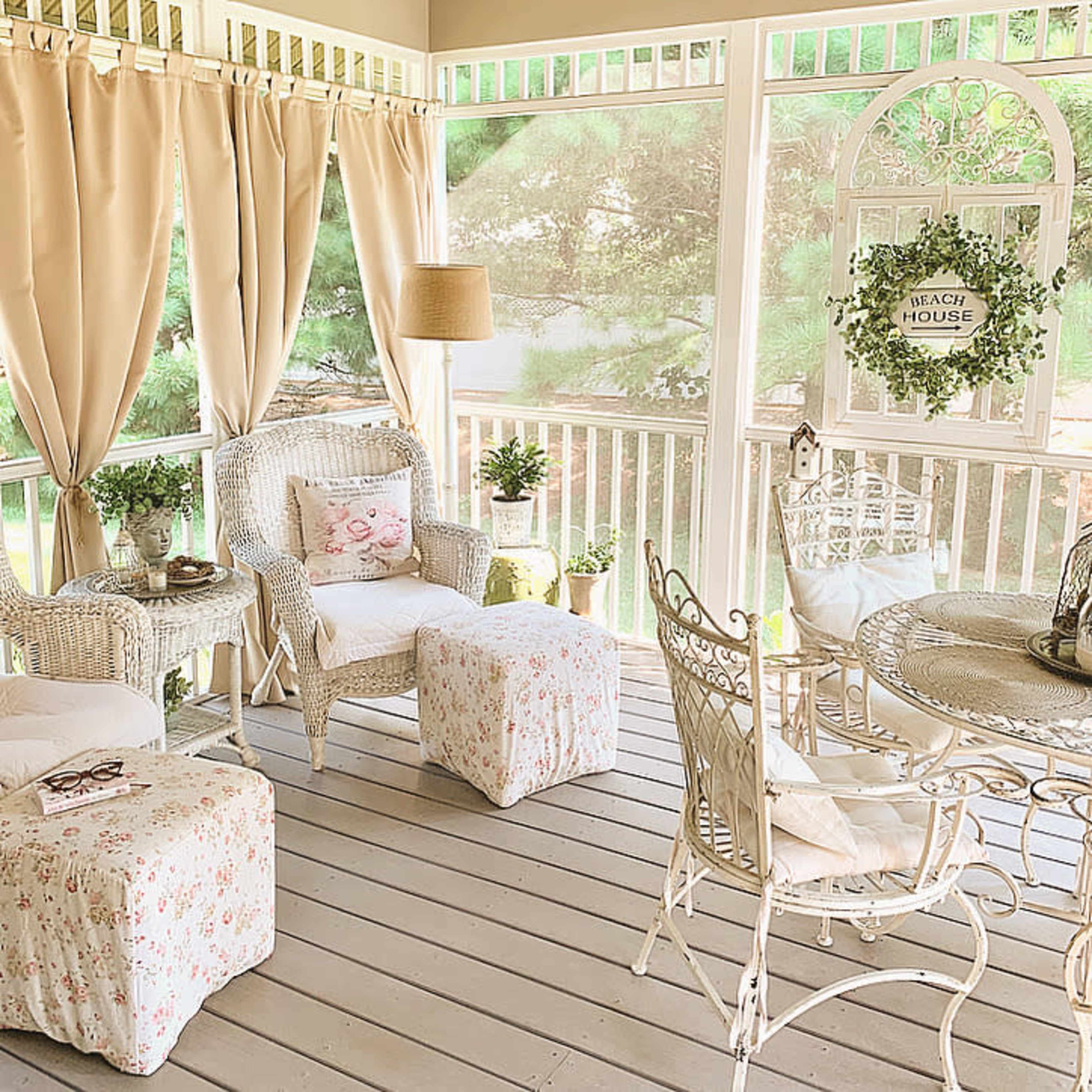 A screened porch with wicker furniture, light curtains, and a round table surrounded by chairs.