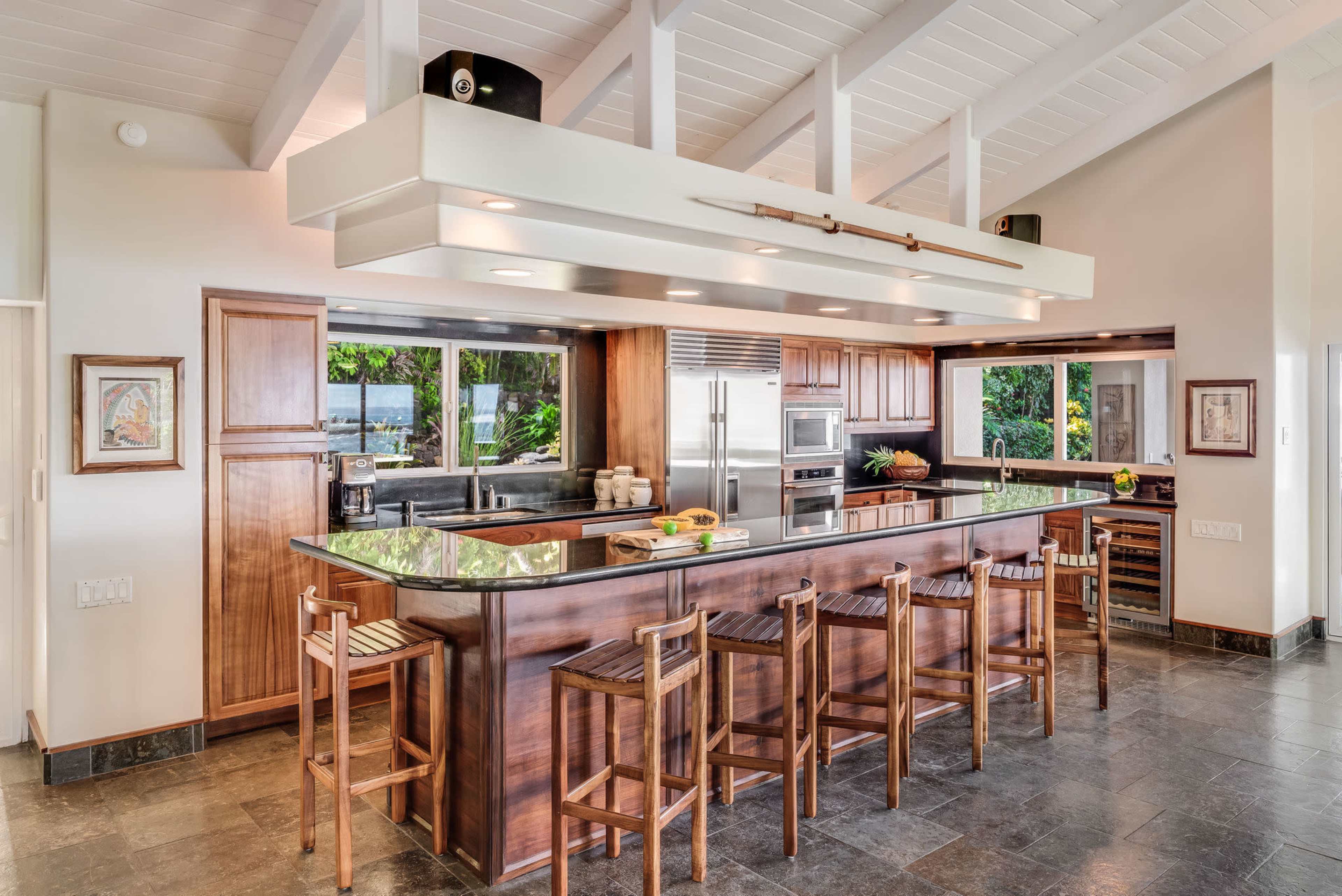 A modern kitchen with a large island, bar seating, and windows that overlook a garden.