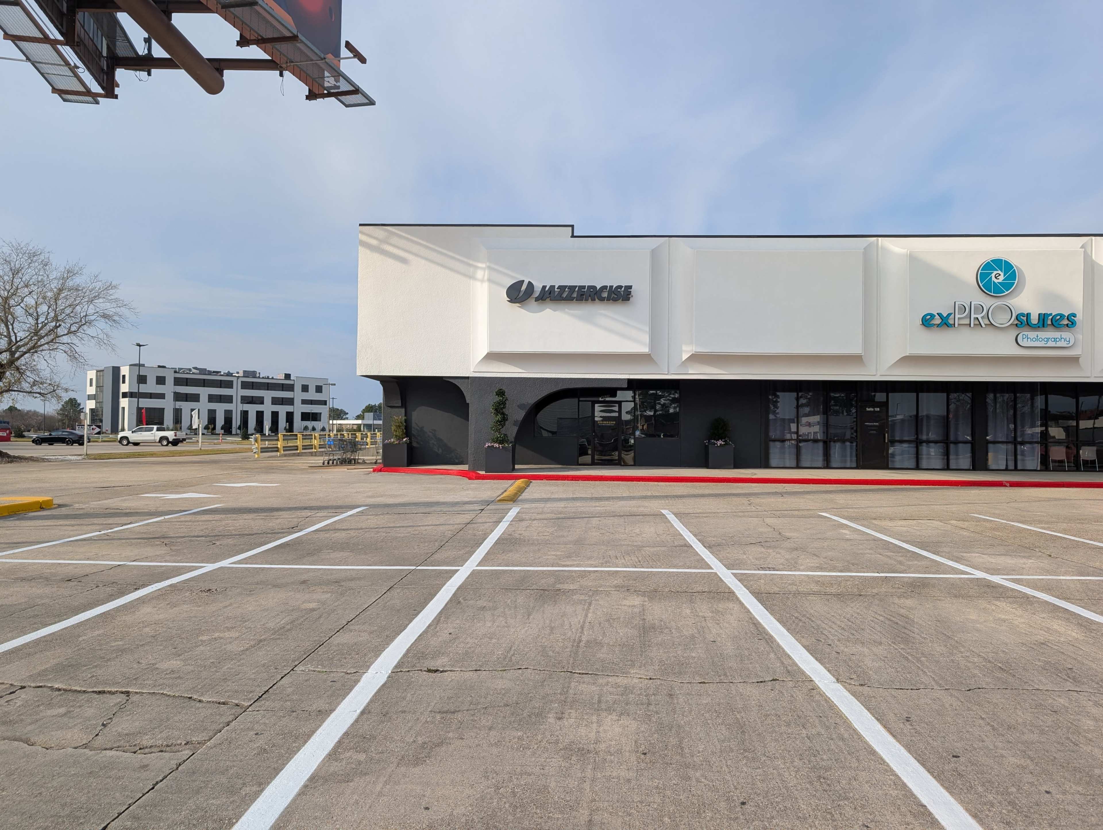 The image shows a view of a commercial building that features a fitness center called "LAZERCIZE" and a wellness center named "exPROsures," situated in a parking lot with clearly marked spaces.