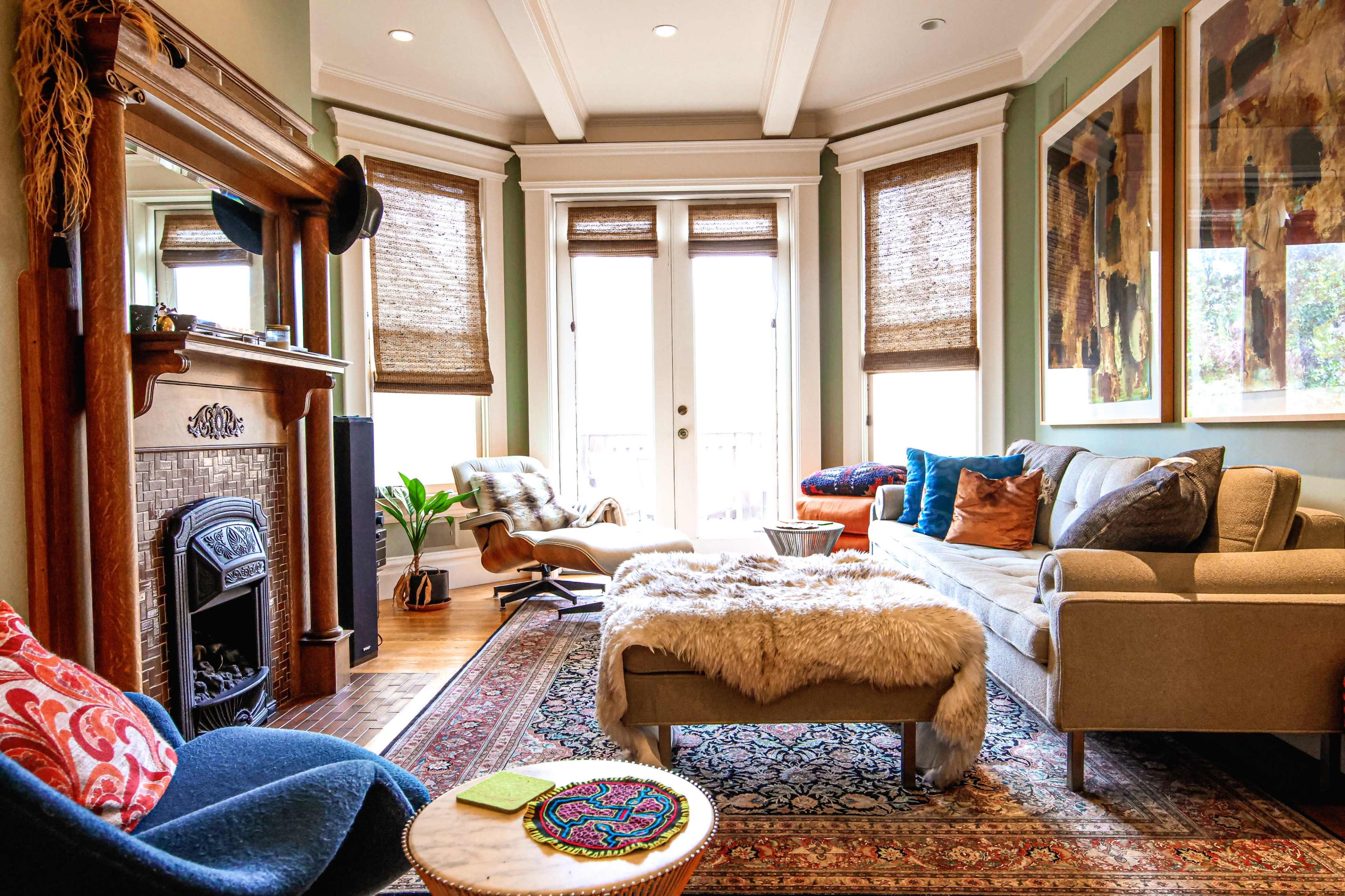 The living room features a cozy seating arrangement with a light-colored sofa, an armchair, a patterned rug, and large windows letting in natural light.