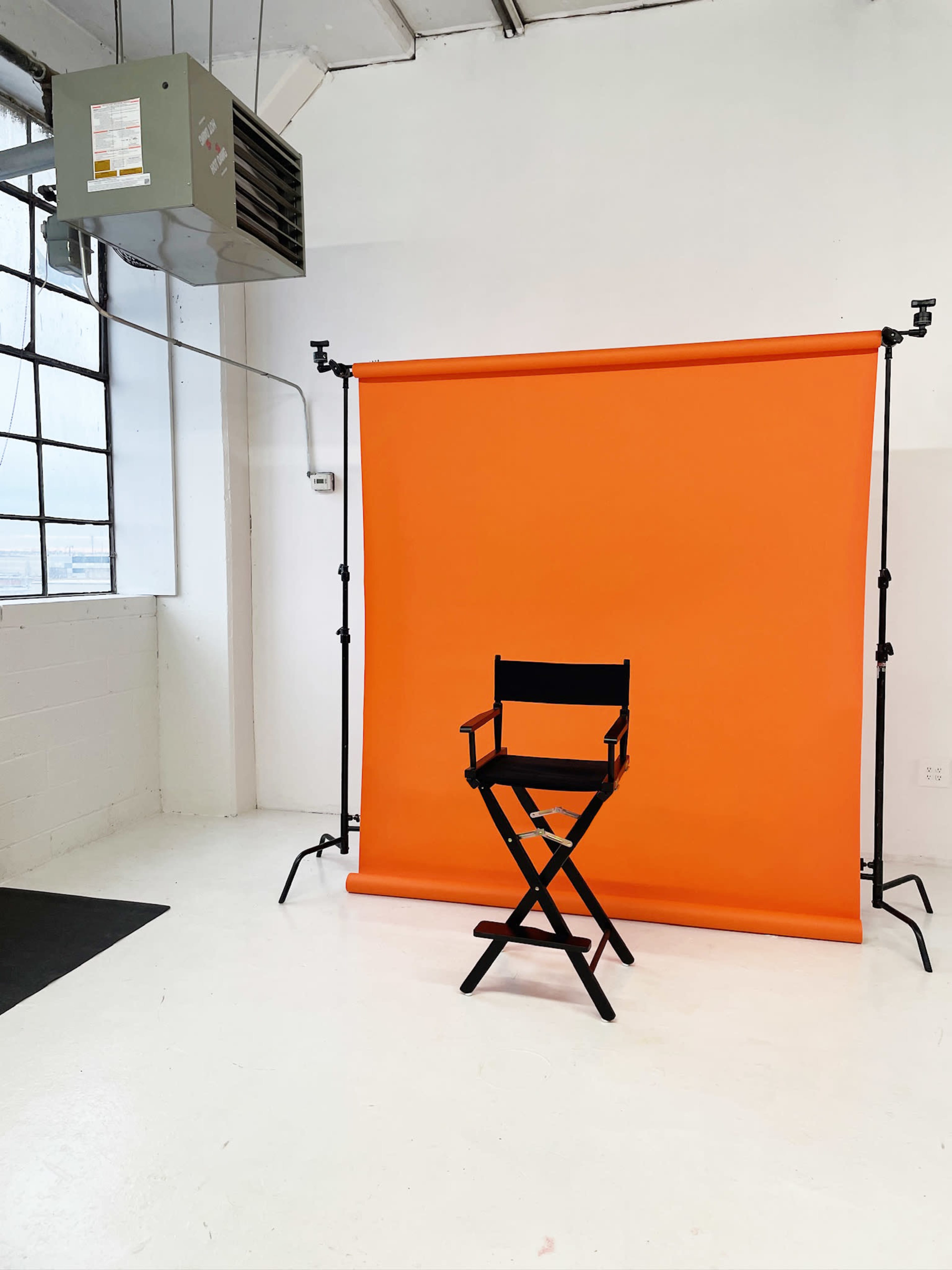 The image shows a black director's chair in front of an orange backdrop in a bright, empty studio space.