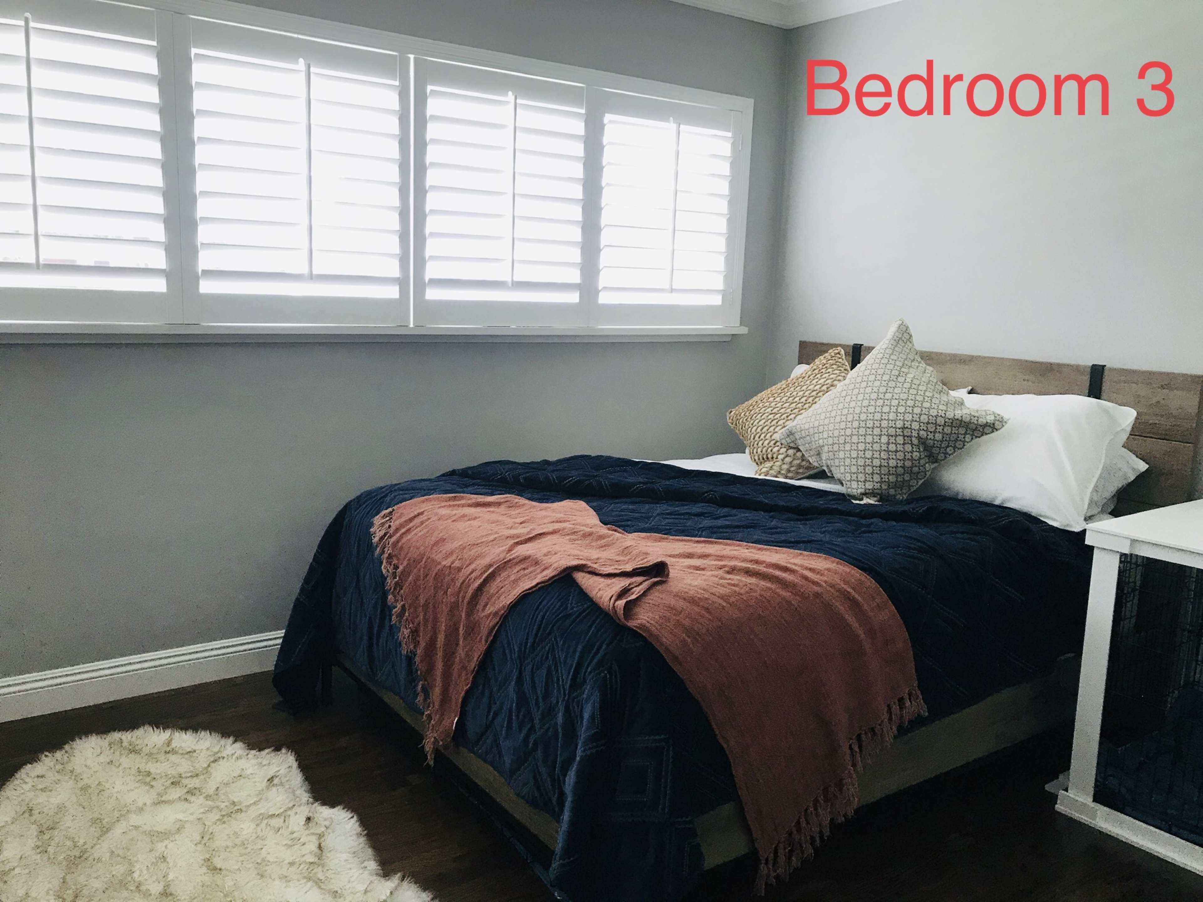 A neatly arranged bedroom features a bed with a navy blue coverlet, accented by two decorative pillows and a throw blanket, alongside a small nightstand and a soft rug on the floor.