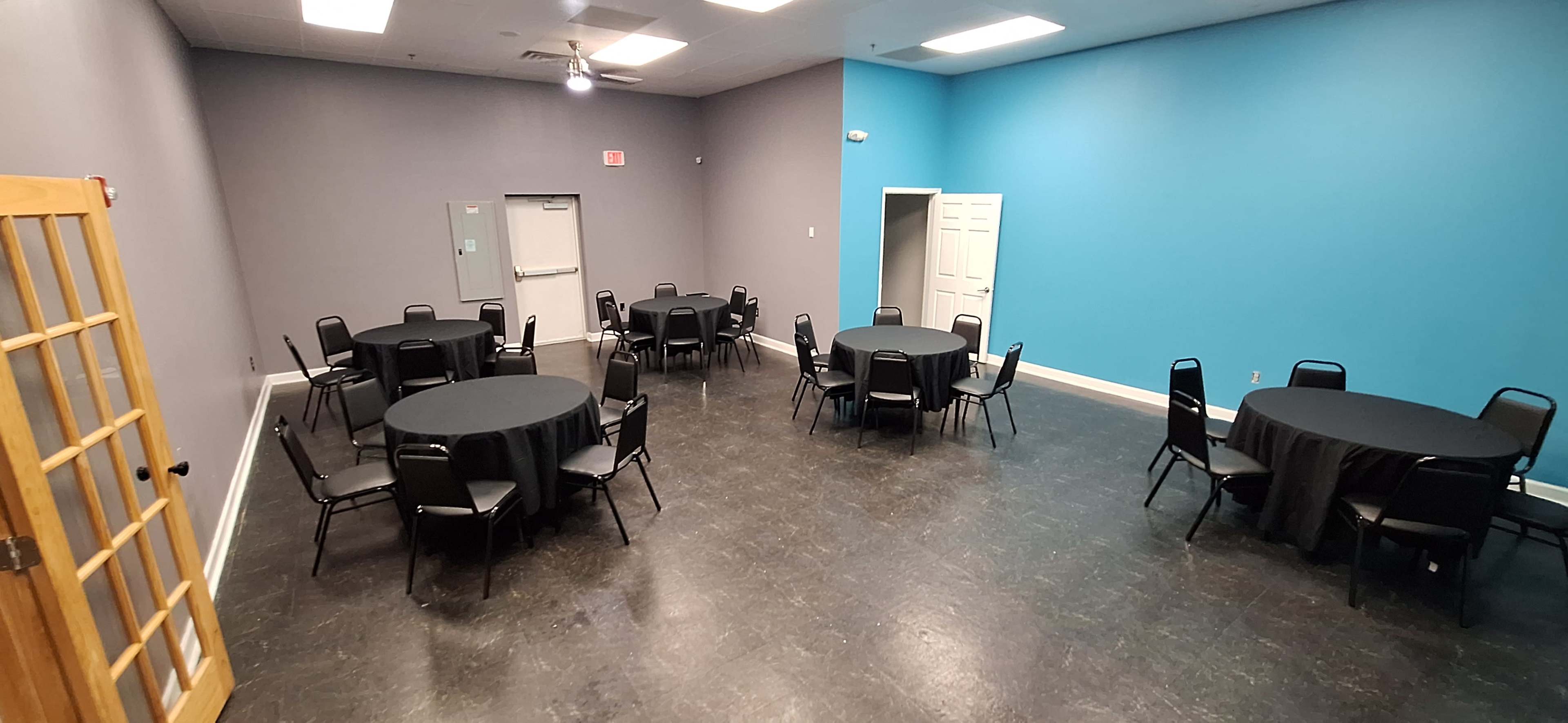 A room with several round tables covered in black tablecloths and arranged around a dark floor, with a teal accent wall.