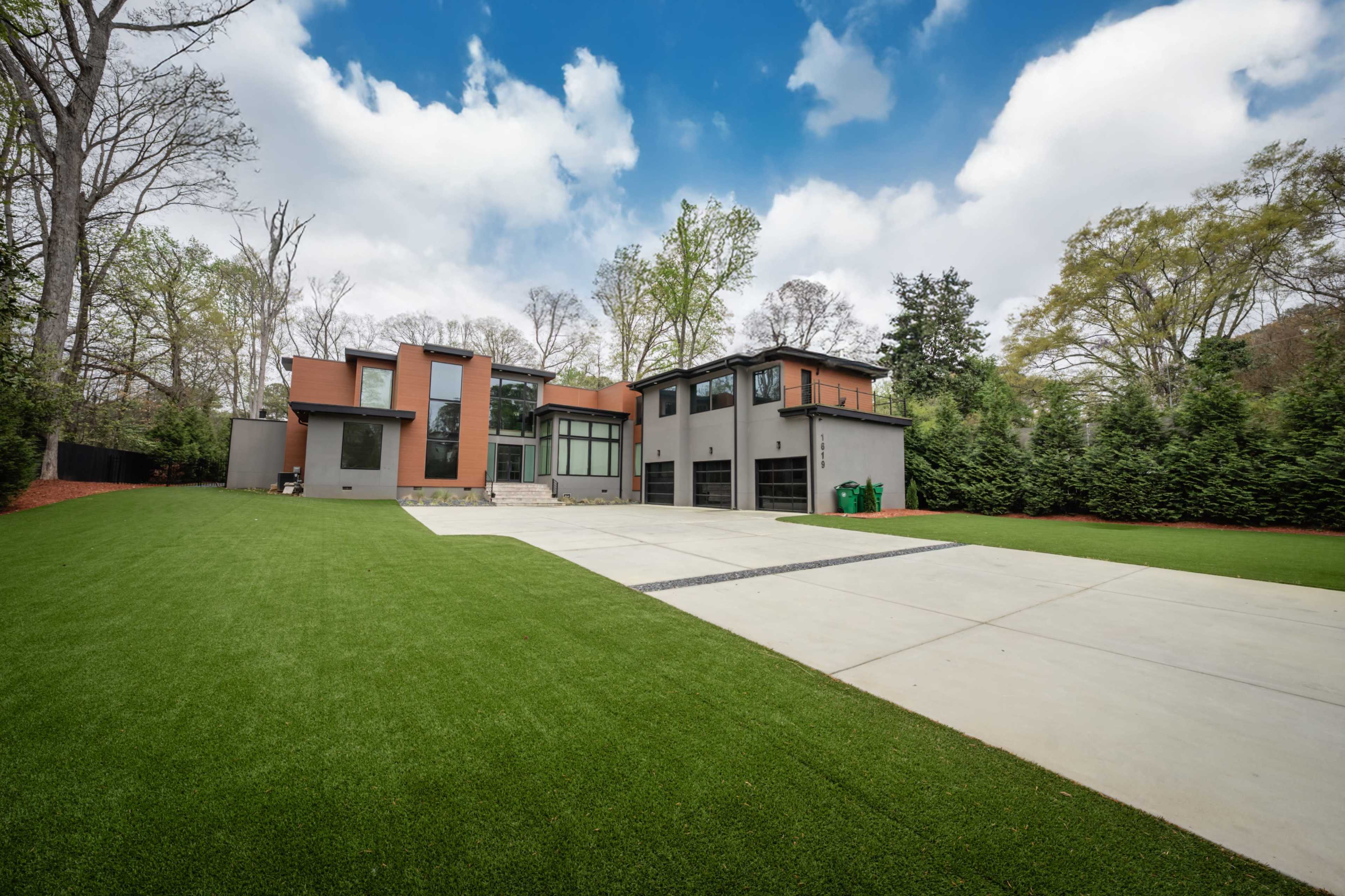 The image shows a modern two-story house with large windows, a landscaped yard, and a driveway made of concrete.