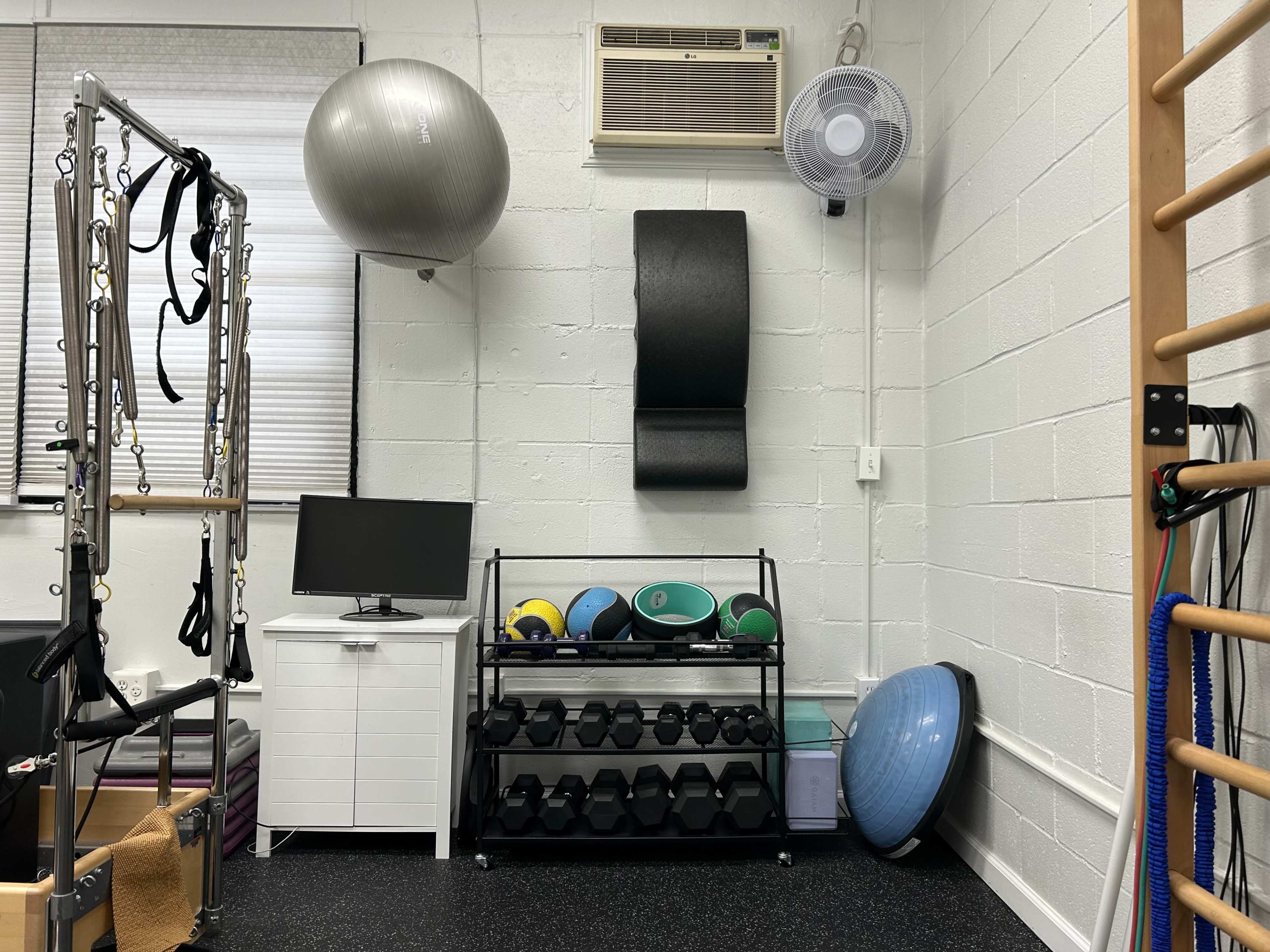 A fitness room equipped with exercise balls, free weights, a fan, a television, and a reformer machine against a textured wall.