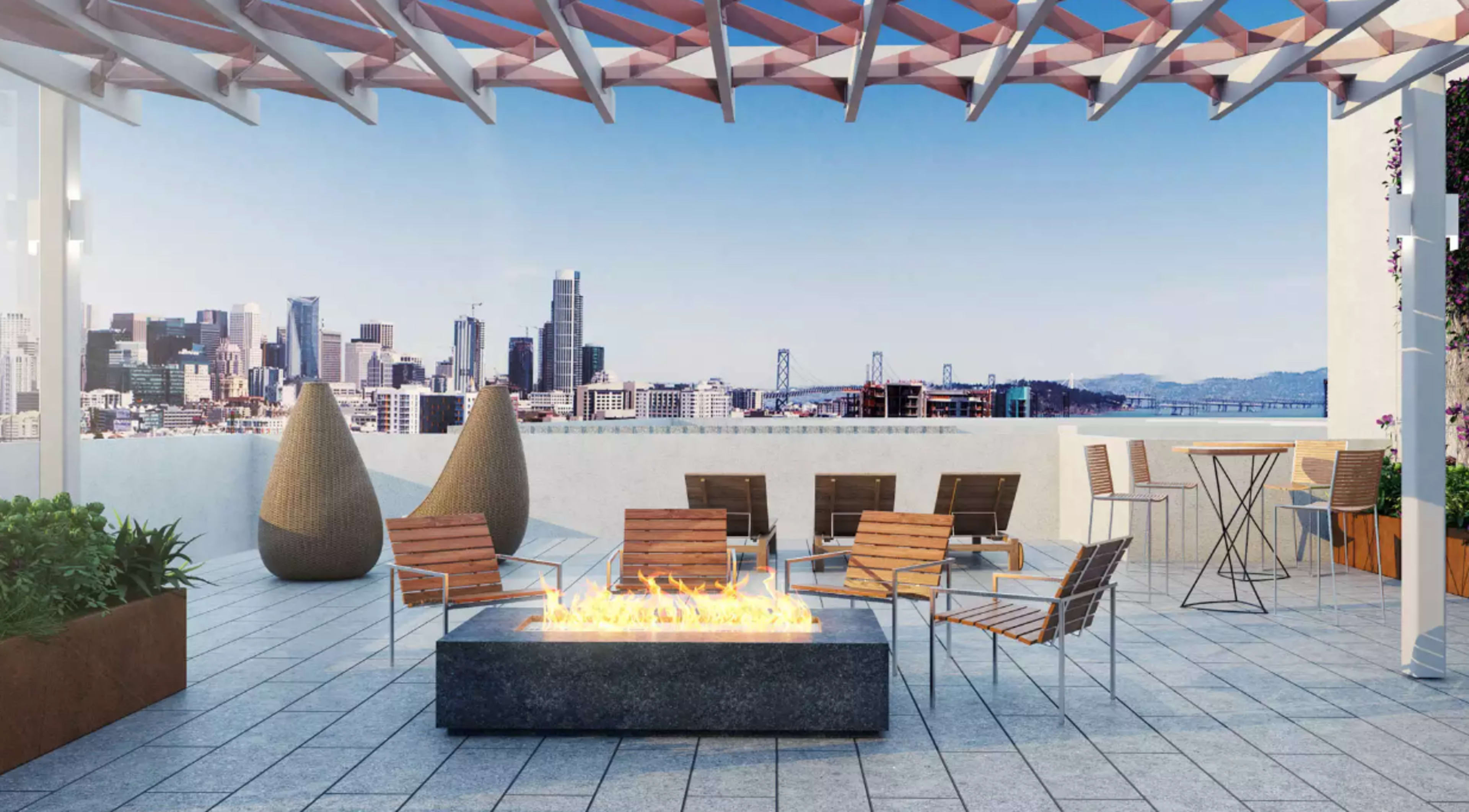 A rooftop terrace with modern seating arrangements, a fire pit, and a skyline view of a city with tall buildings.
