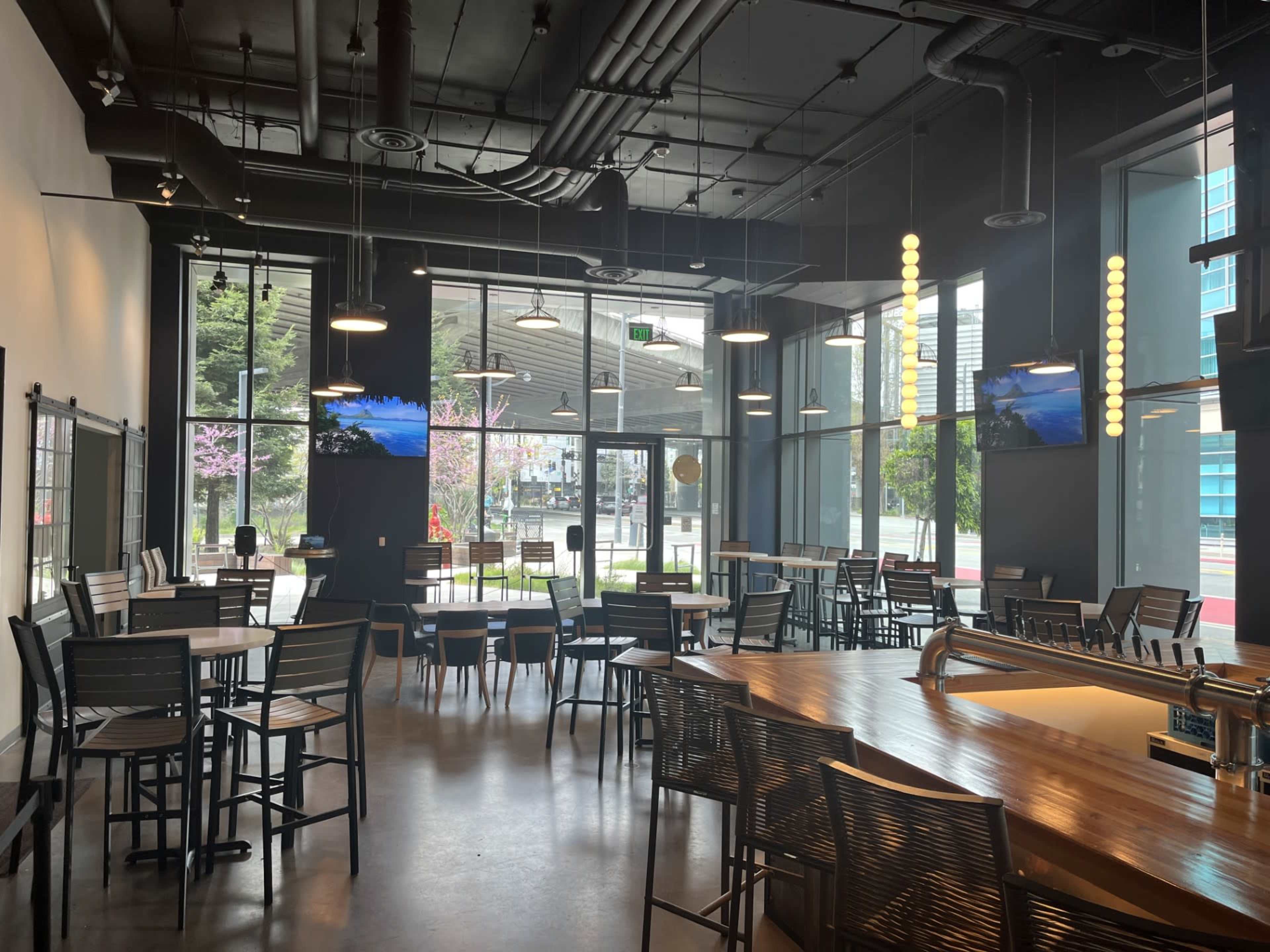 The image shows a modern restaurant interior with large windows, seating areas, and two mounted televisions.
