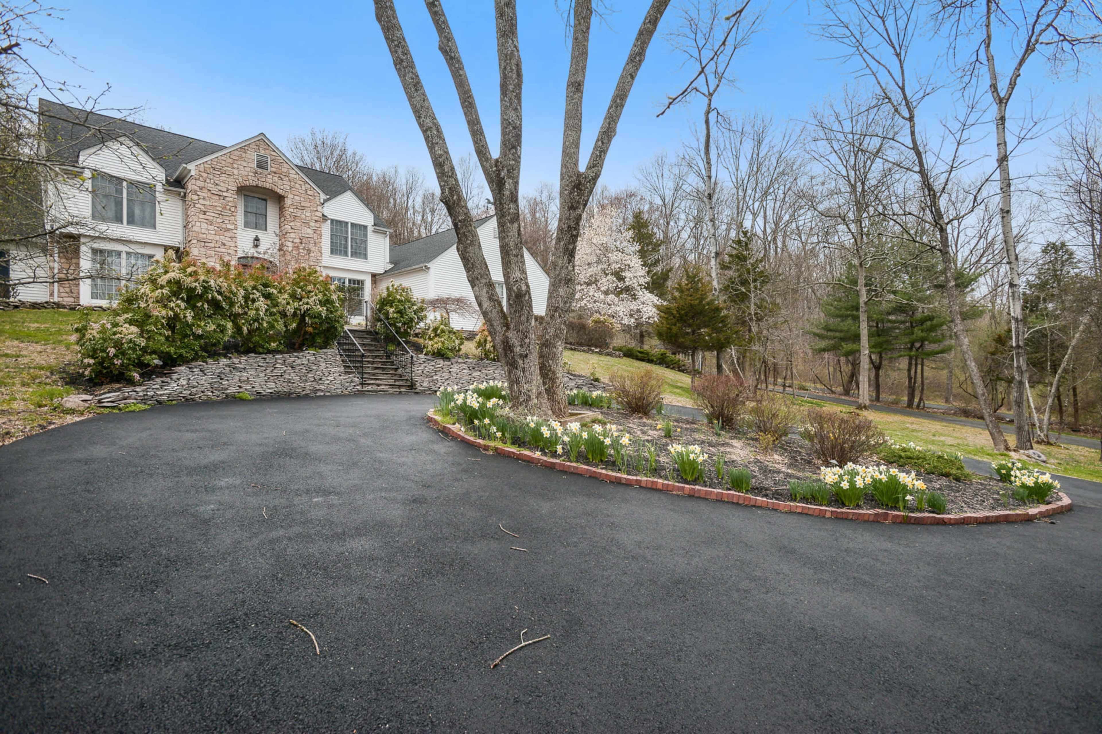 A circular driveway with a flower bed surrounds a home set against a backdrop of bare trees.