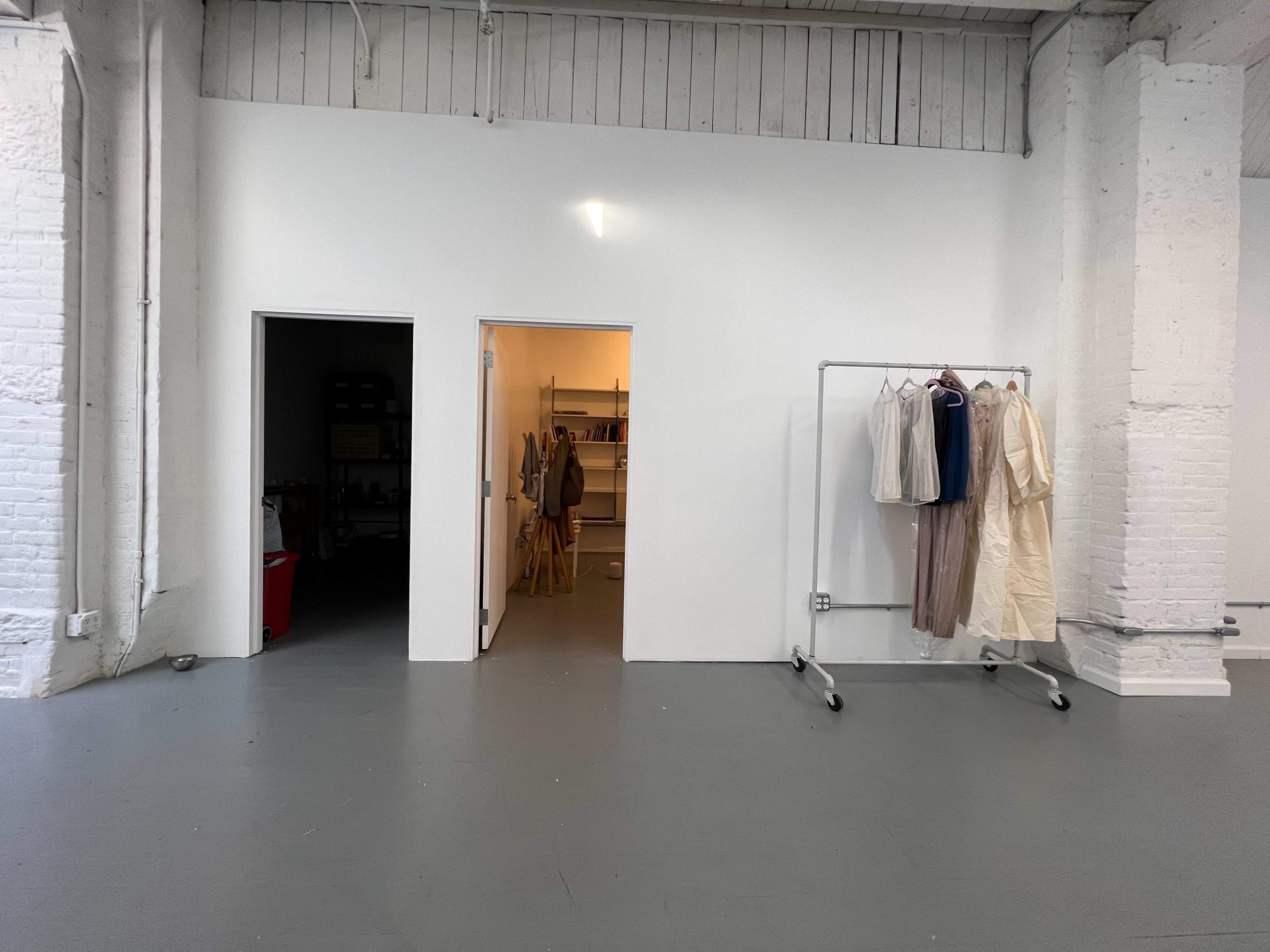 A minimalist interior space featuring two doorways, a clothing rack with several garments, and a light-colored floor.