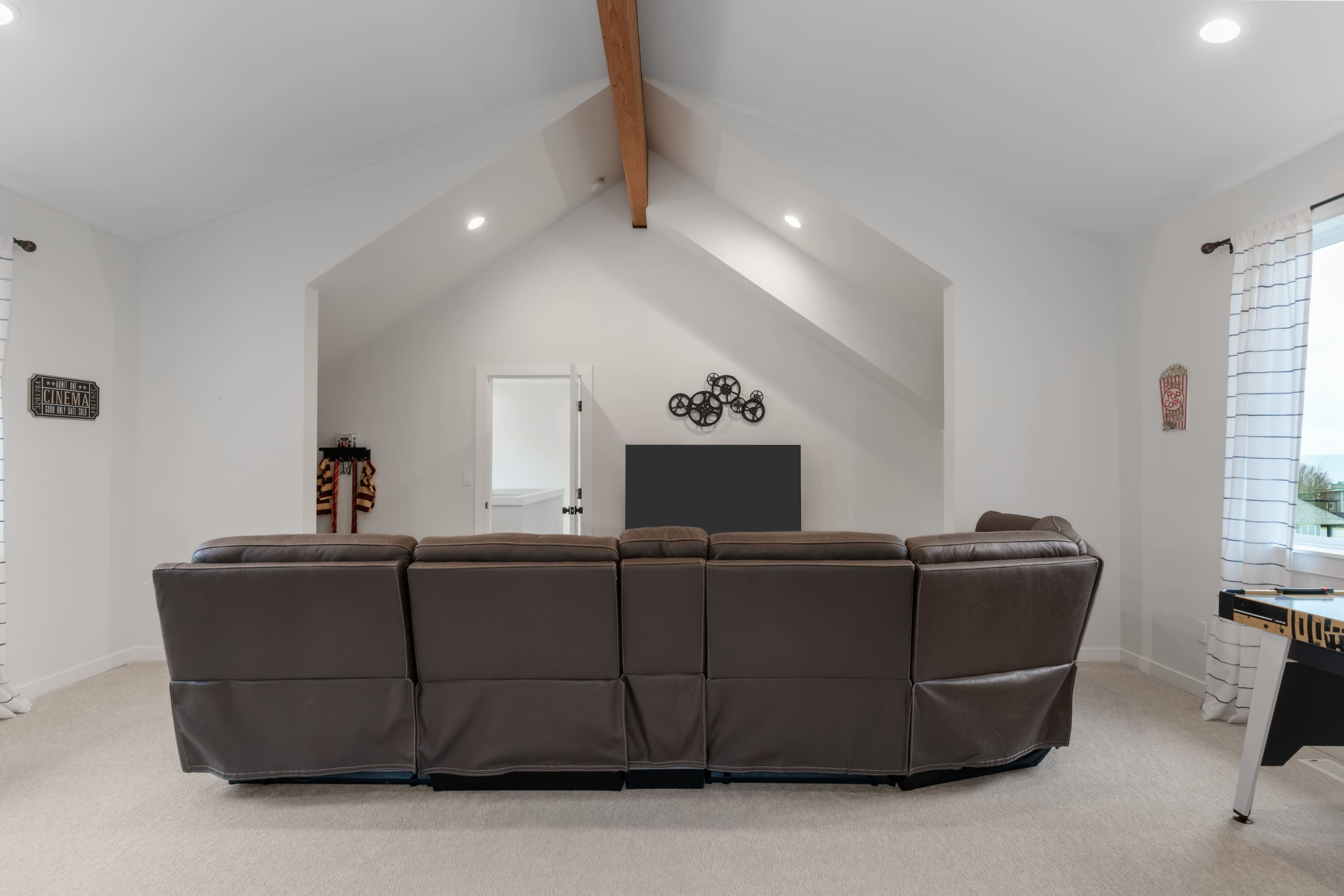 A spacious living room featuring a brown sectional sofa facing a wall with no visible decorations, and a doorway leading to another room.