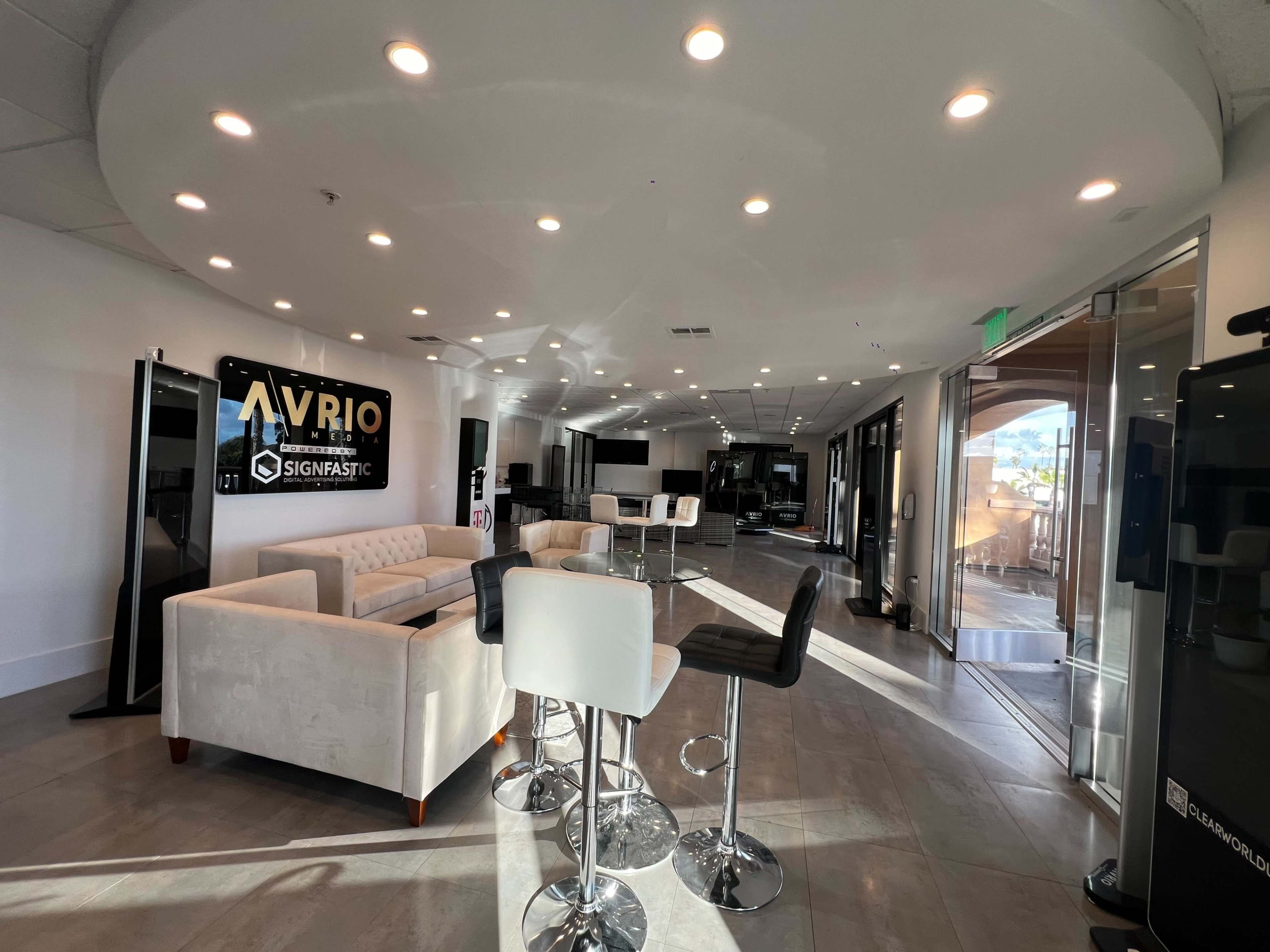 A modern open space with a seating area featuring a white sofa and bar stools, illuminated by circular ceiling lights.