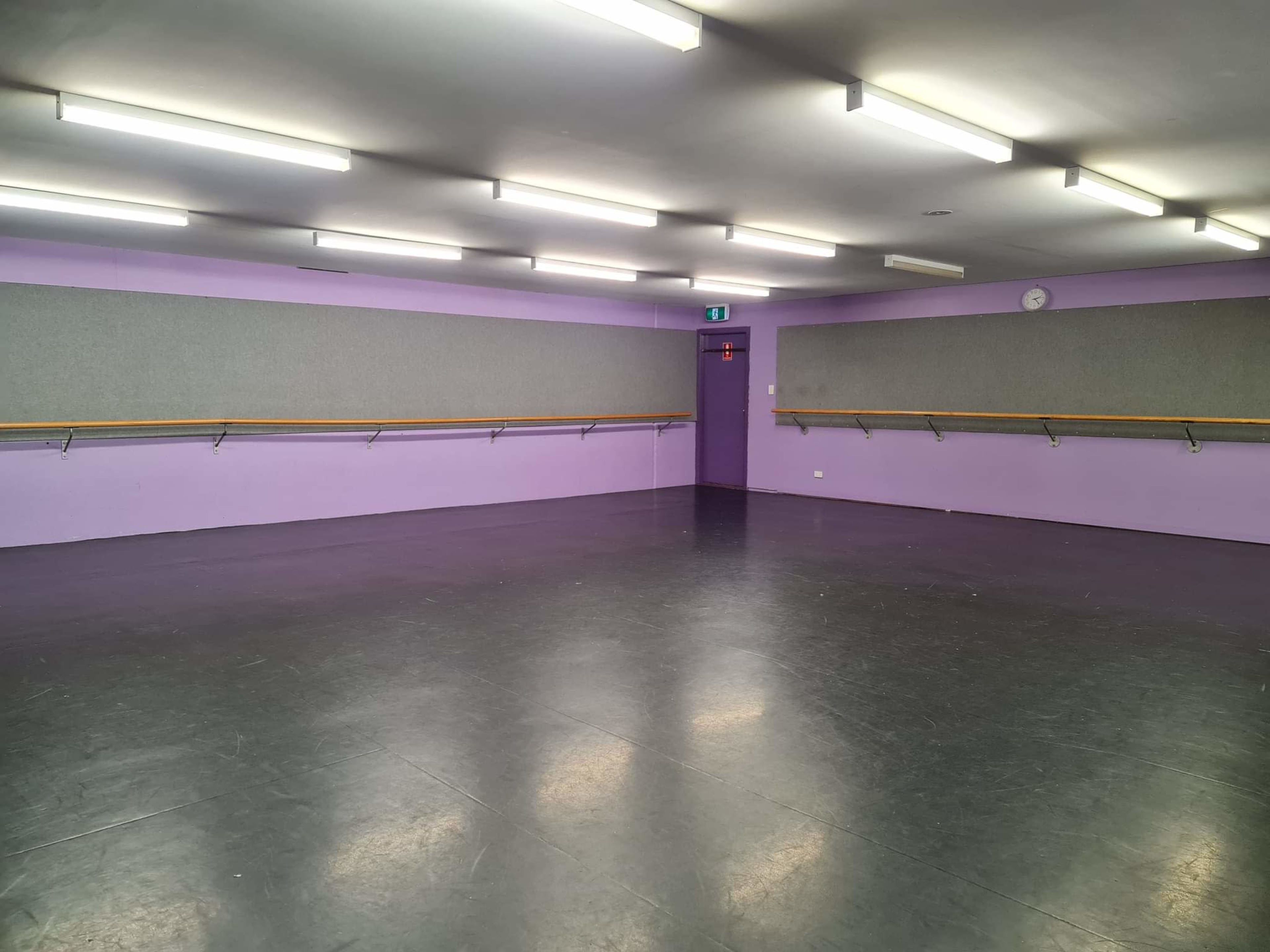 An empty dance studio with purple walls, a smooth black floor, and mirrored panels along the walls.