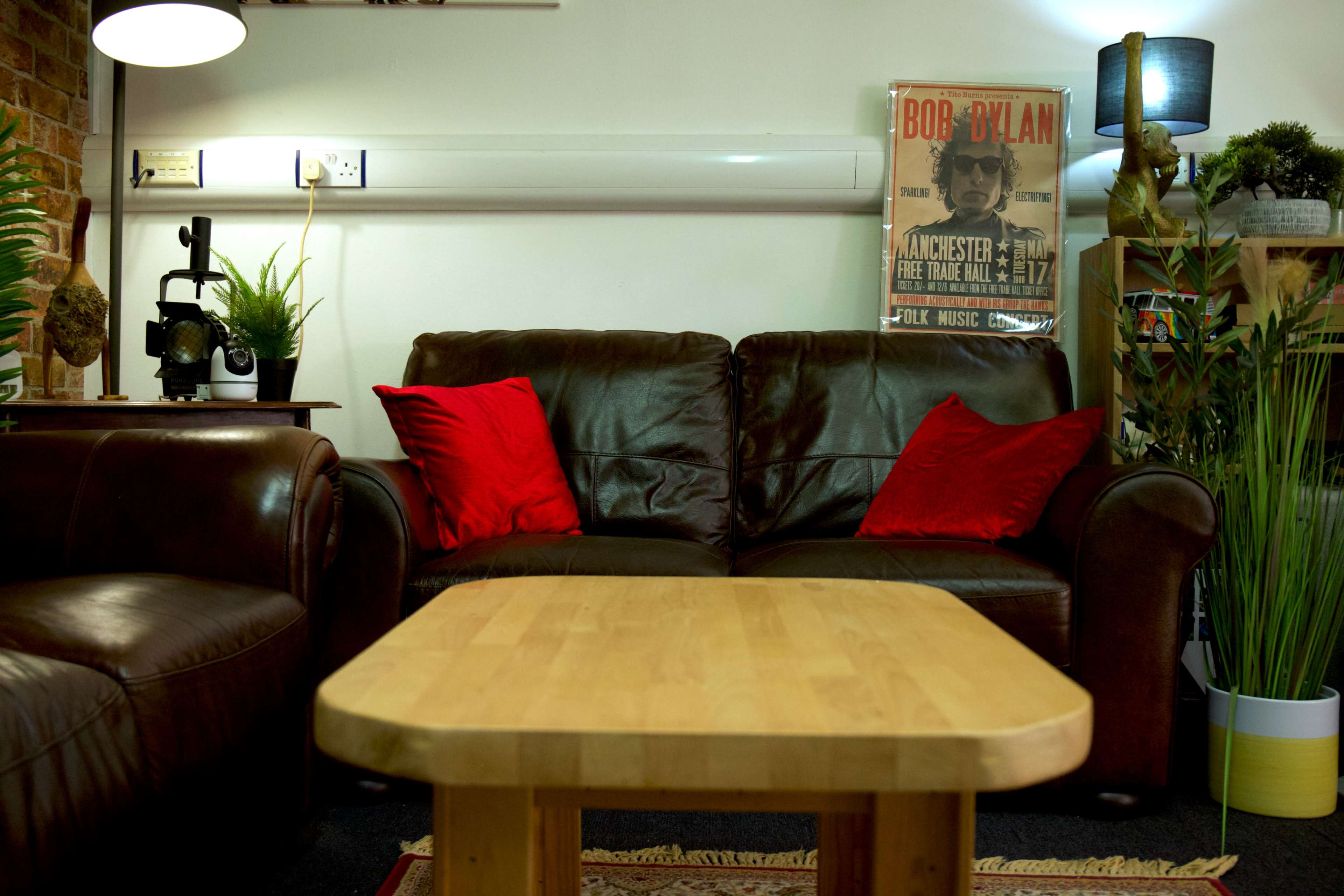 The image shows a cozy living room with dark leather sofas, a wooden coffee table, and a Bob Dylan poster on the wall.