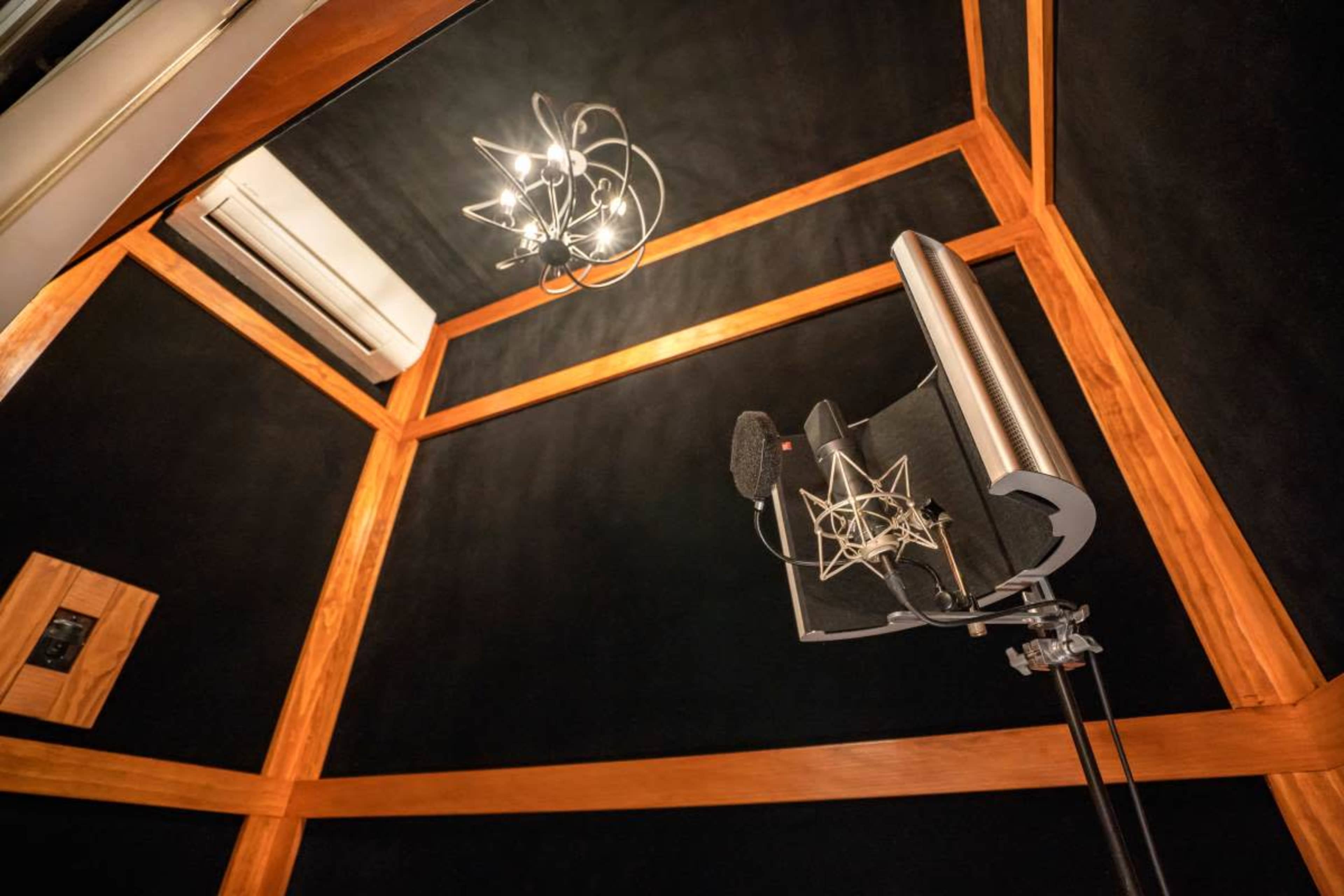 The image shows the interior of a soundproof recording booth with a microphone, acoustic treatments, and a ceiling light fixture.