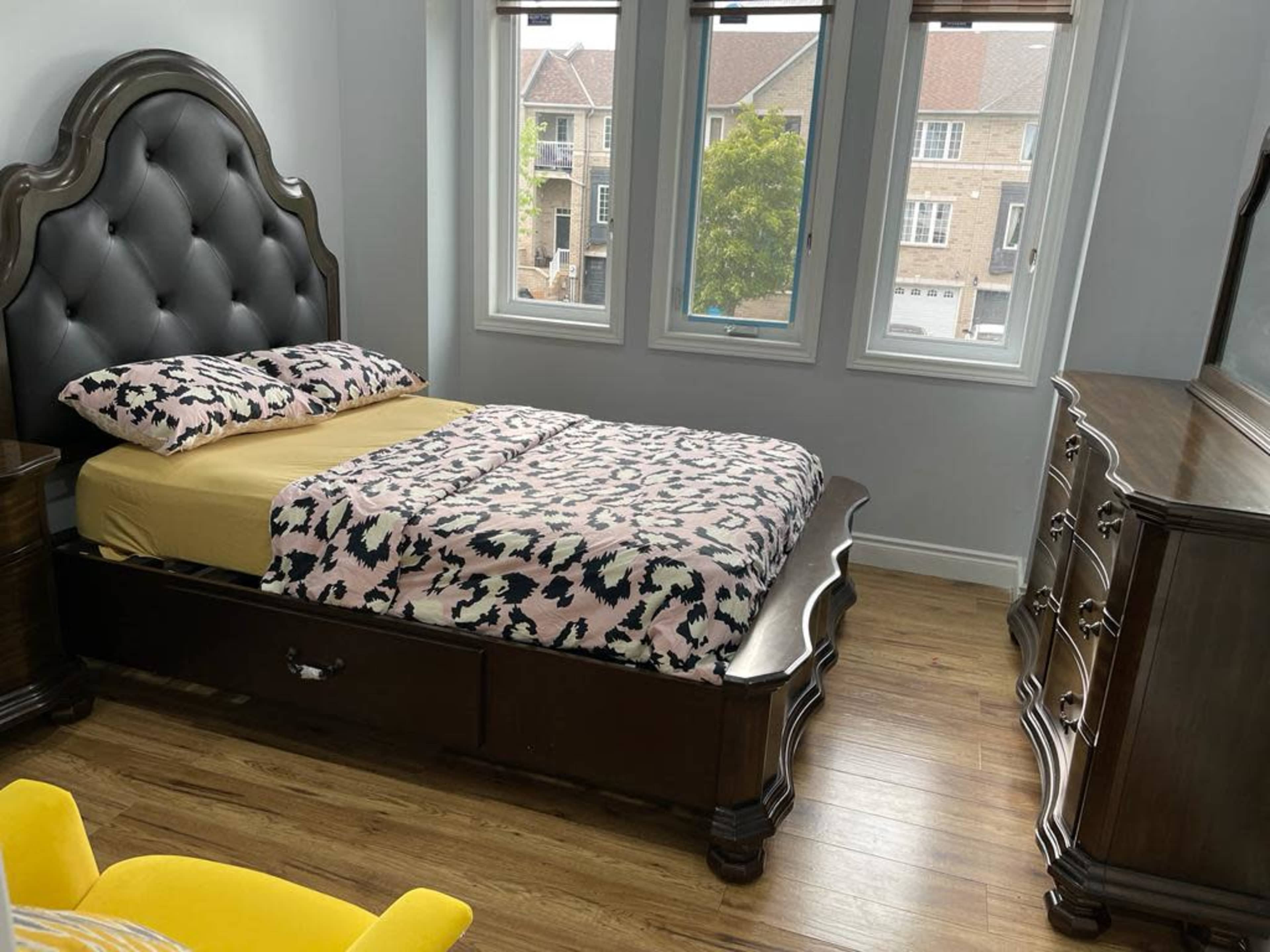 A bedroom featuring a wooden bed with a decorative headboard, a dresser, and large windows letting in natural light.