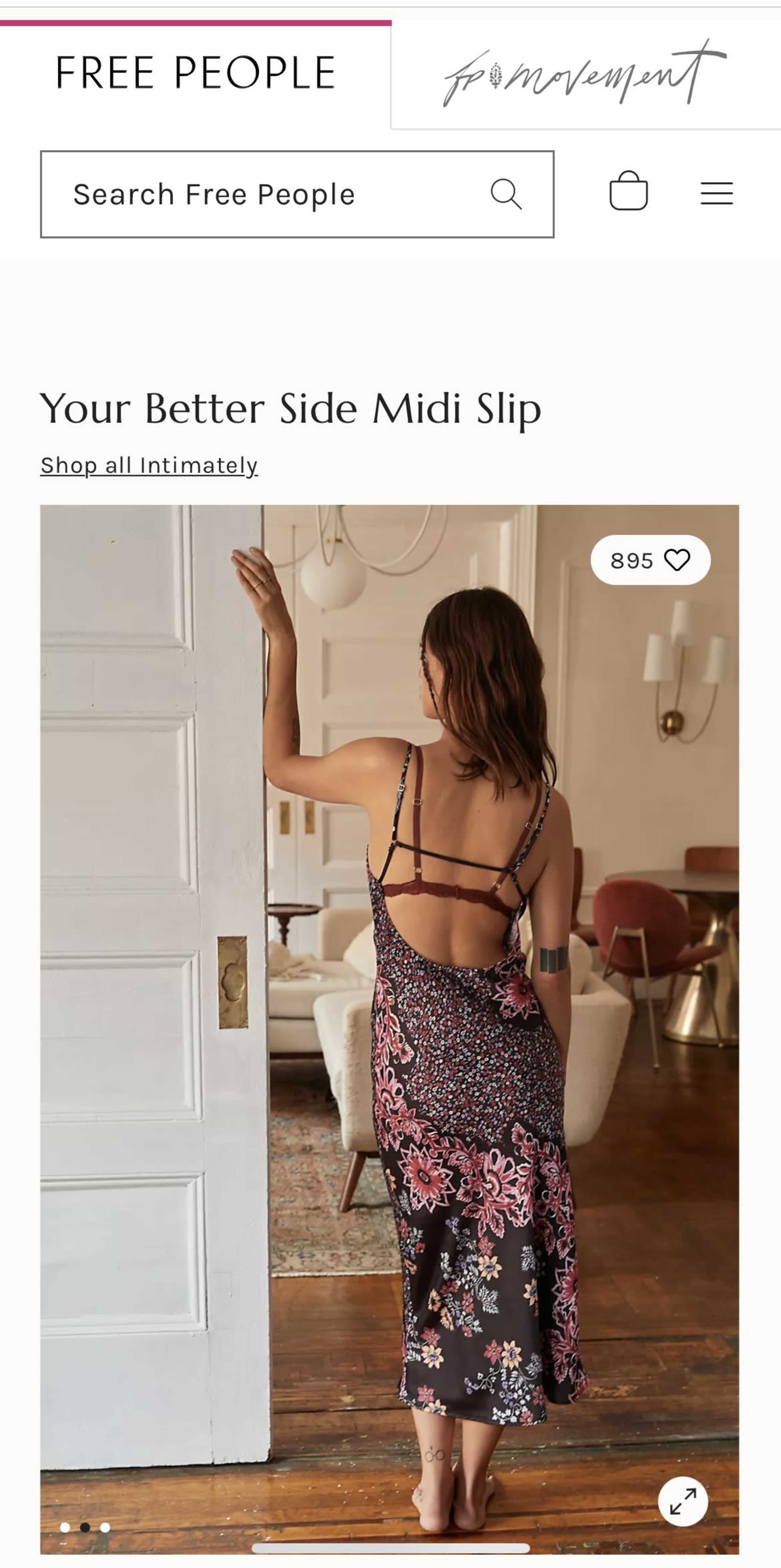 A woman stands with her back to the camera, wearing a floral midi slip dress, in a tastefully decorated room with vintage furniture.