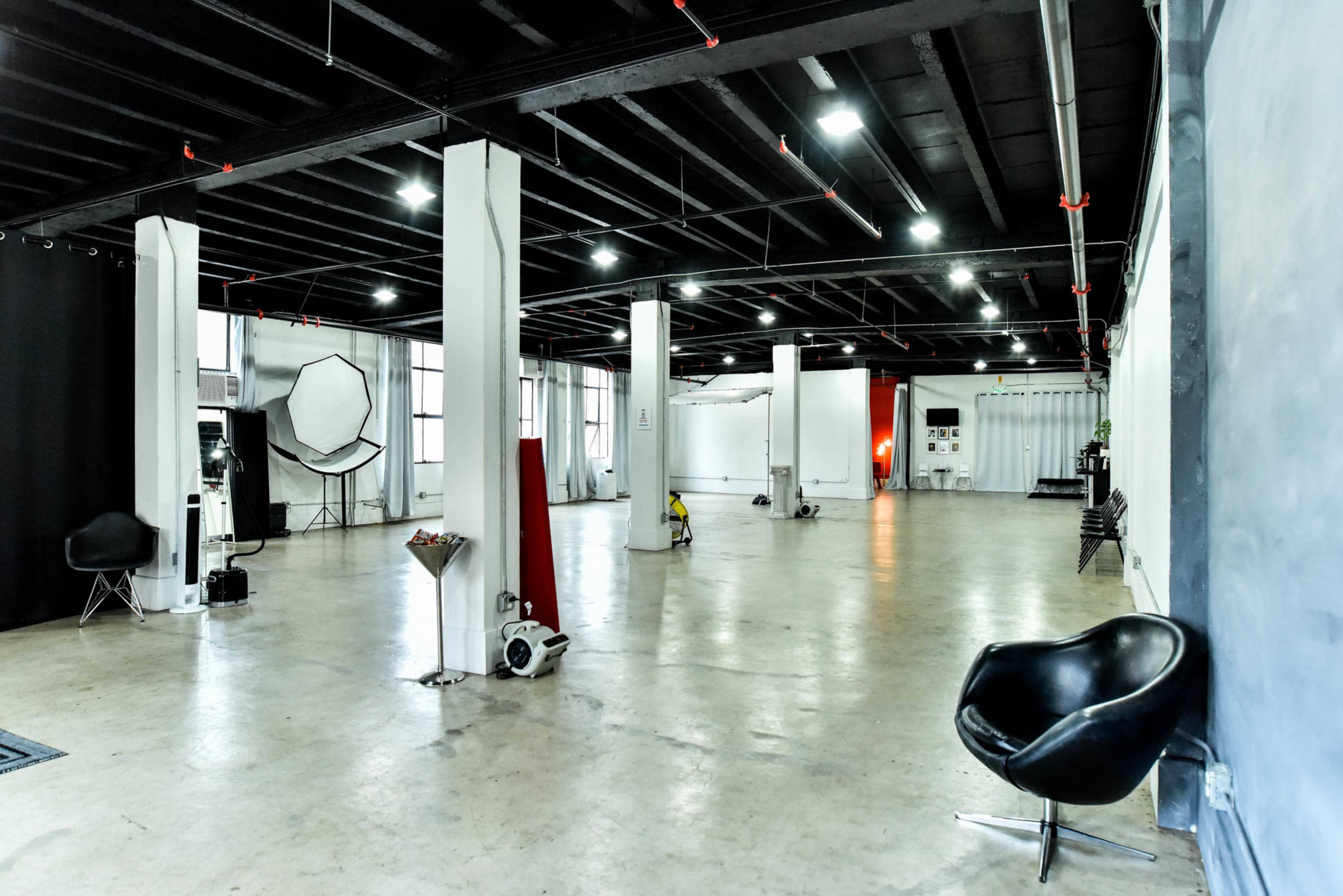 The image shows a spacious, empty photography studio with high ceilings and various photography equipment positioned throughout.