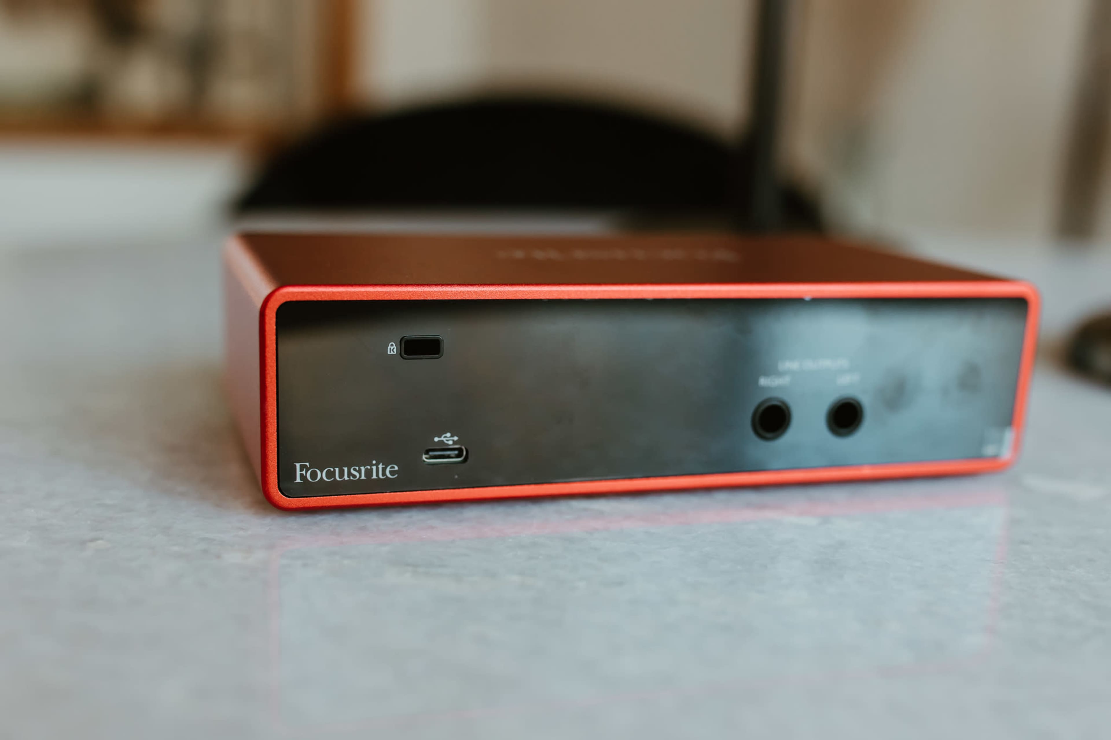 The image shows a red and black Focusrite audio interface positioned on a light gray surface.