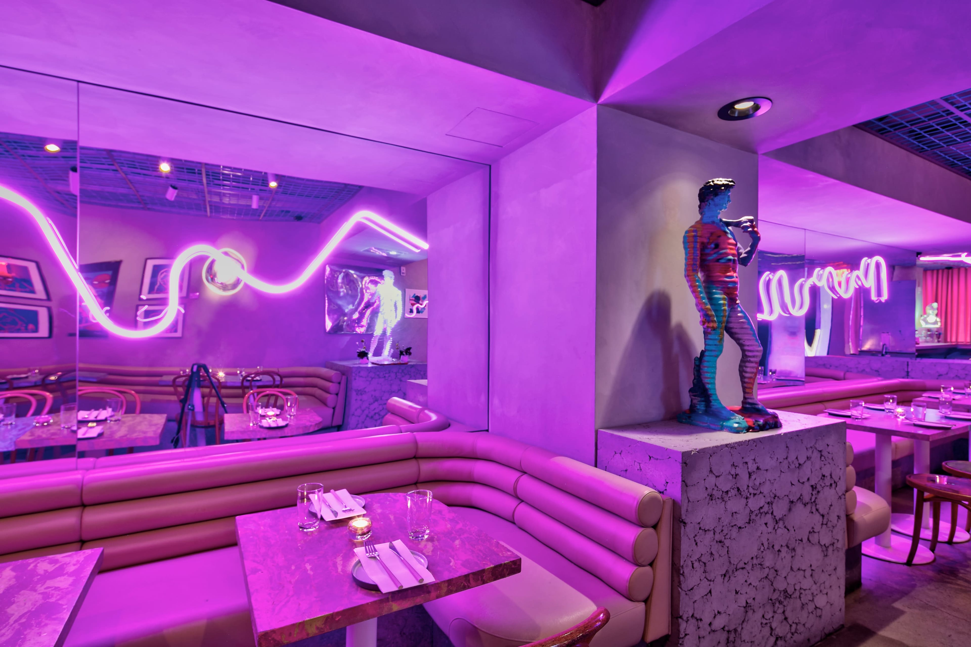 The image shows a vibrant restaurant interior with purple neon lights, modern sculptures, and stylish seating arrangements.