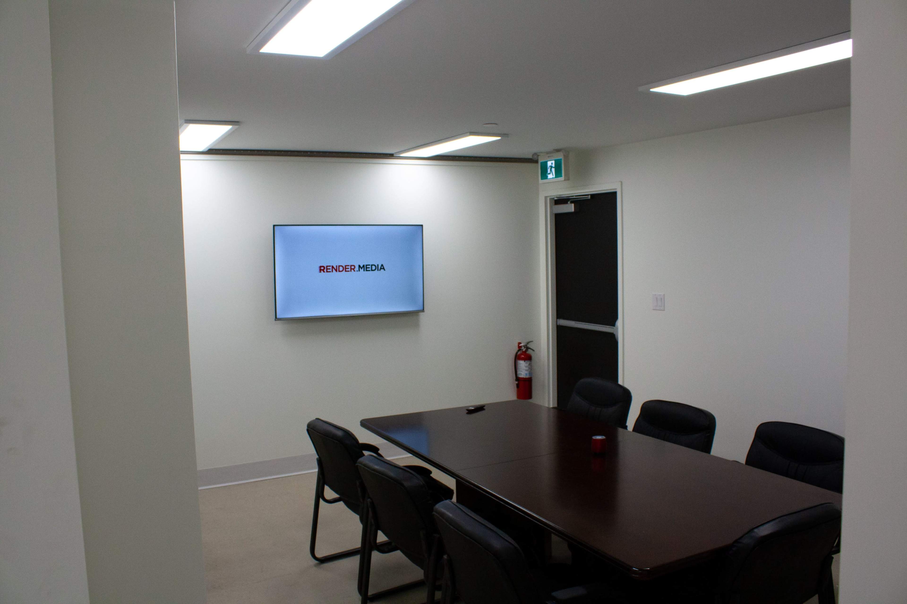 A conference room features a long wooden table surrounded by black chairs, with a screen displaying the logo "RENDER MEDIA" on the wall.