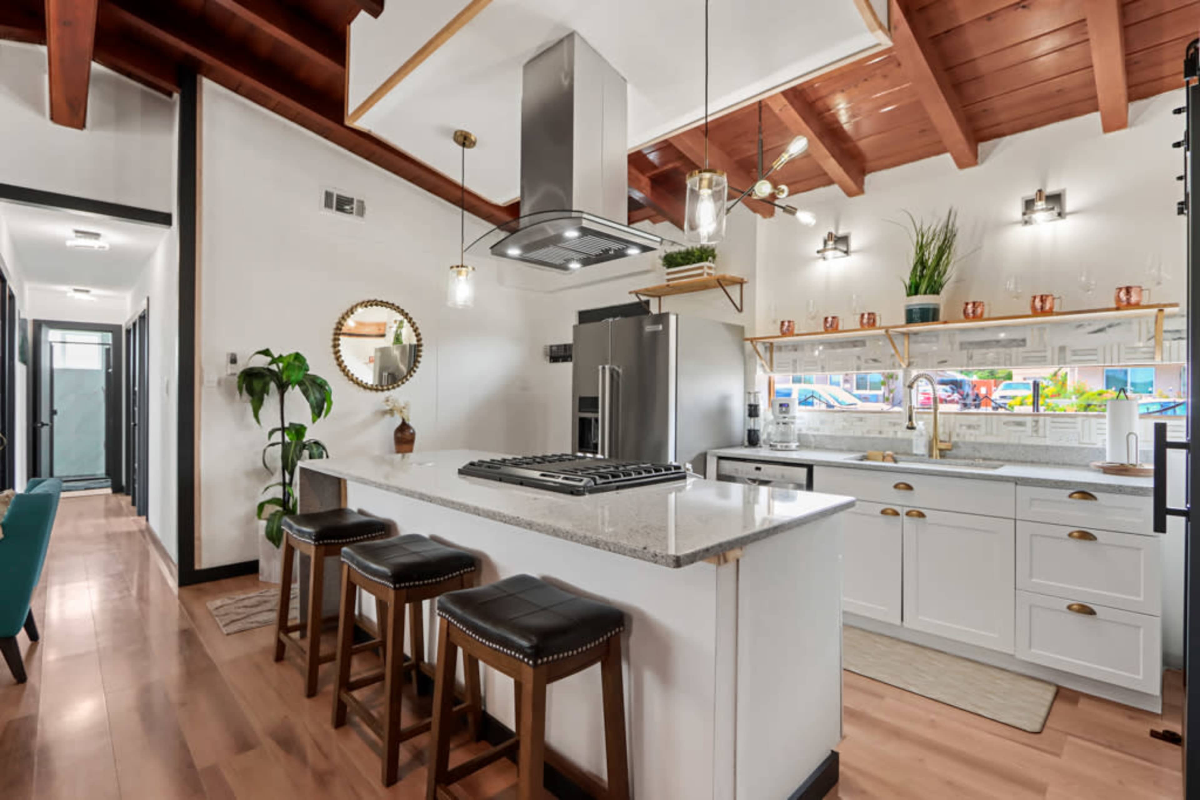 A modern kitchen features a large island with seating, stainless steel appliances, and wooden ceilings with exposed beams.