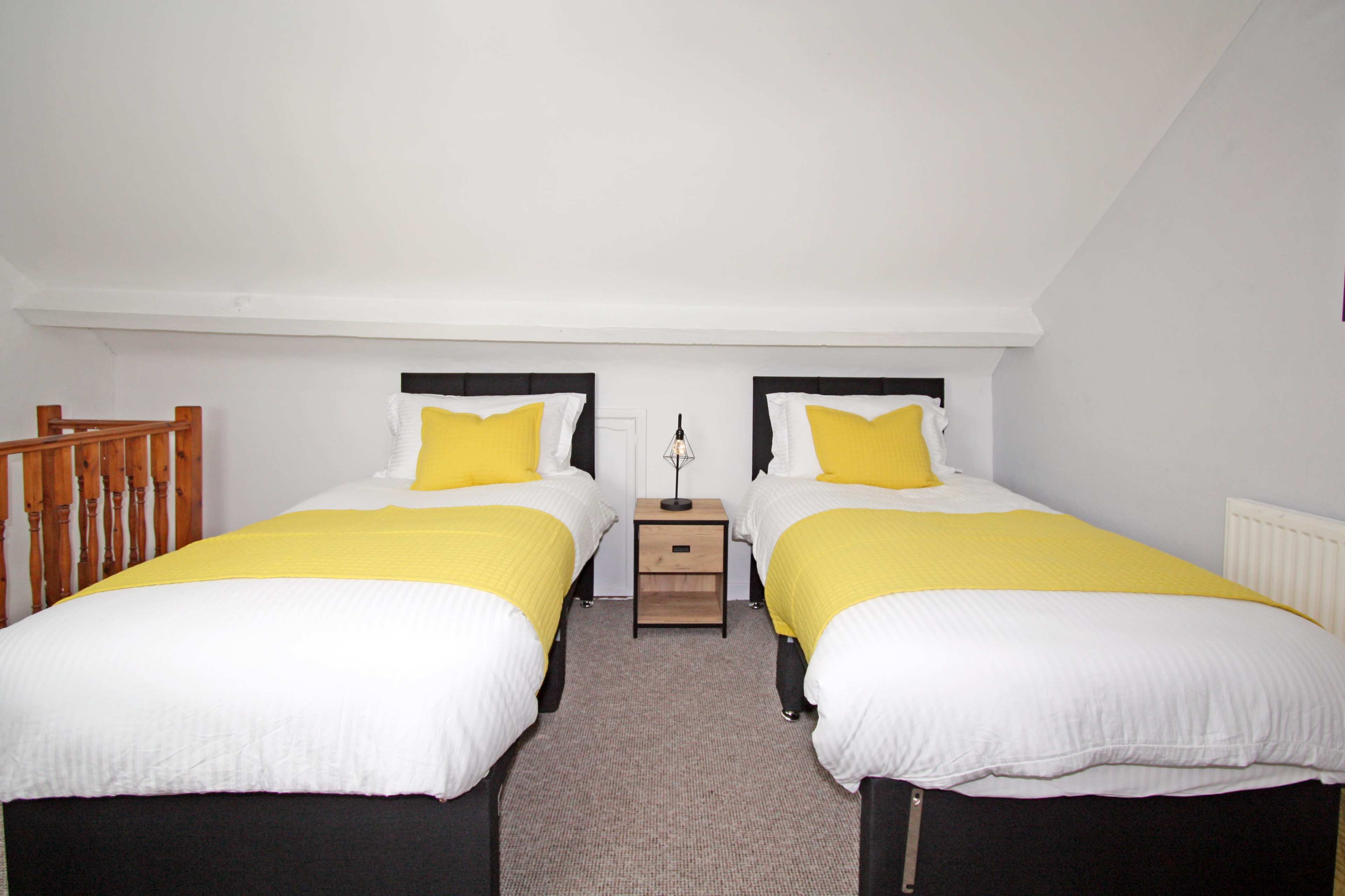 The image shows a bedroom with two single beds, each topped with a yellow blanket, separated by a small nightstand.