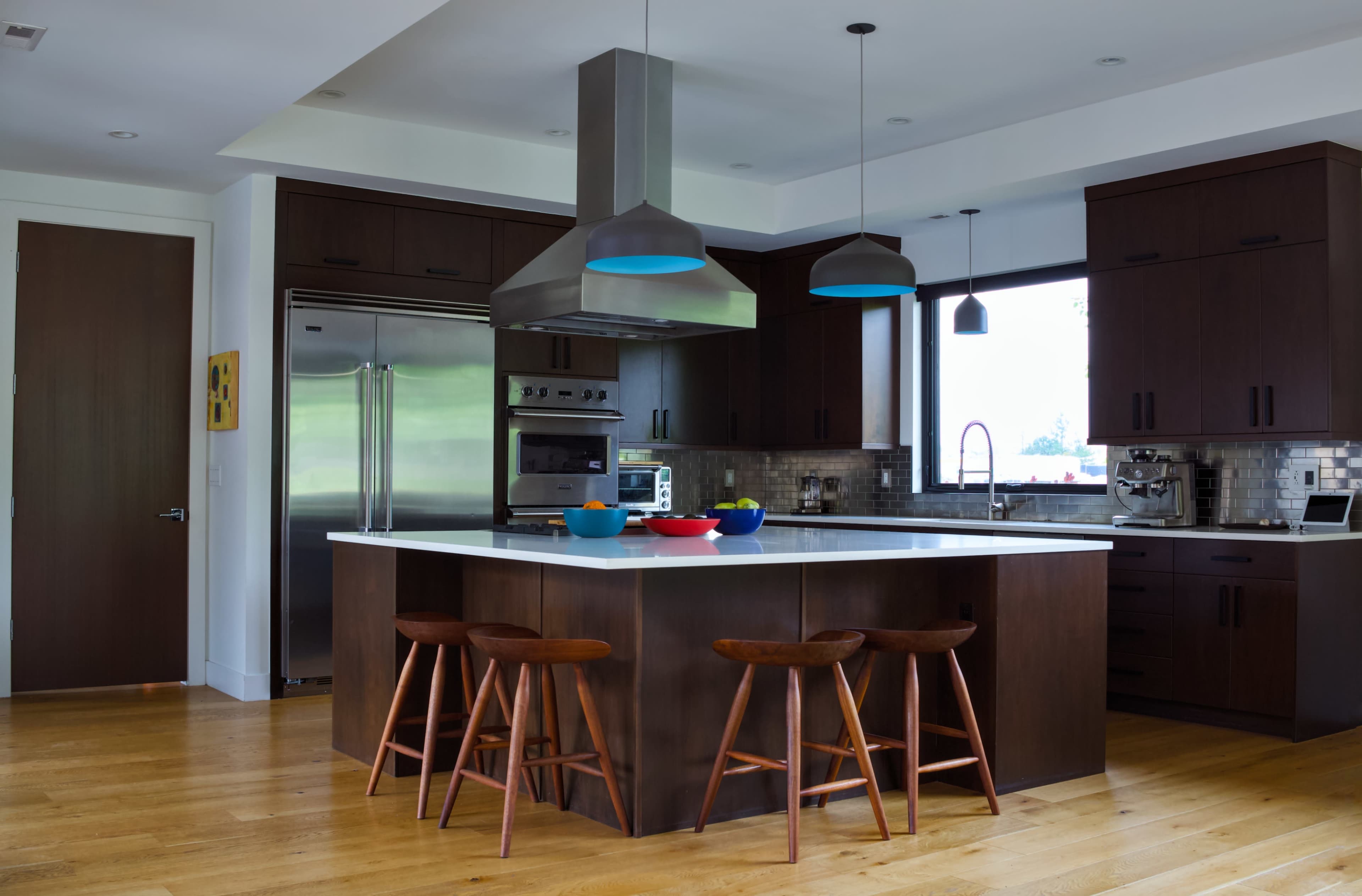 The image shows a modern kitchen featuring dark cabinetry, a large island with wooden stools, and stainless steel appliances.