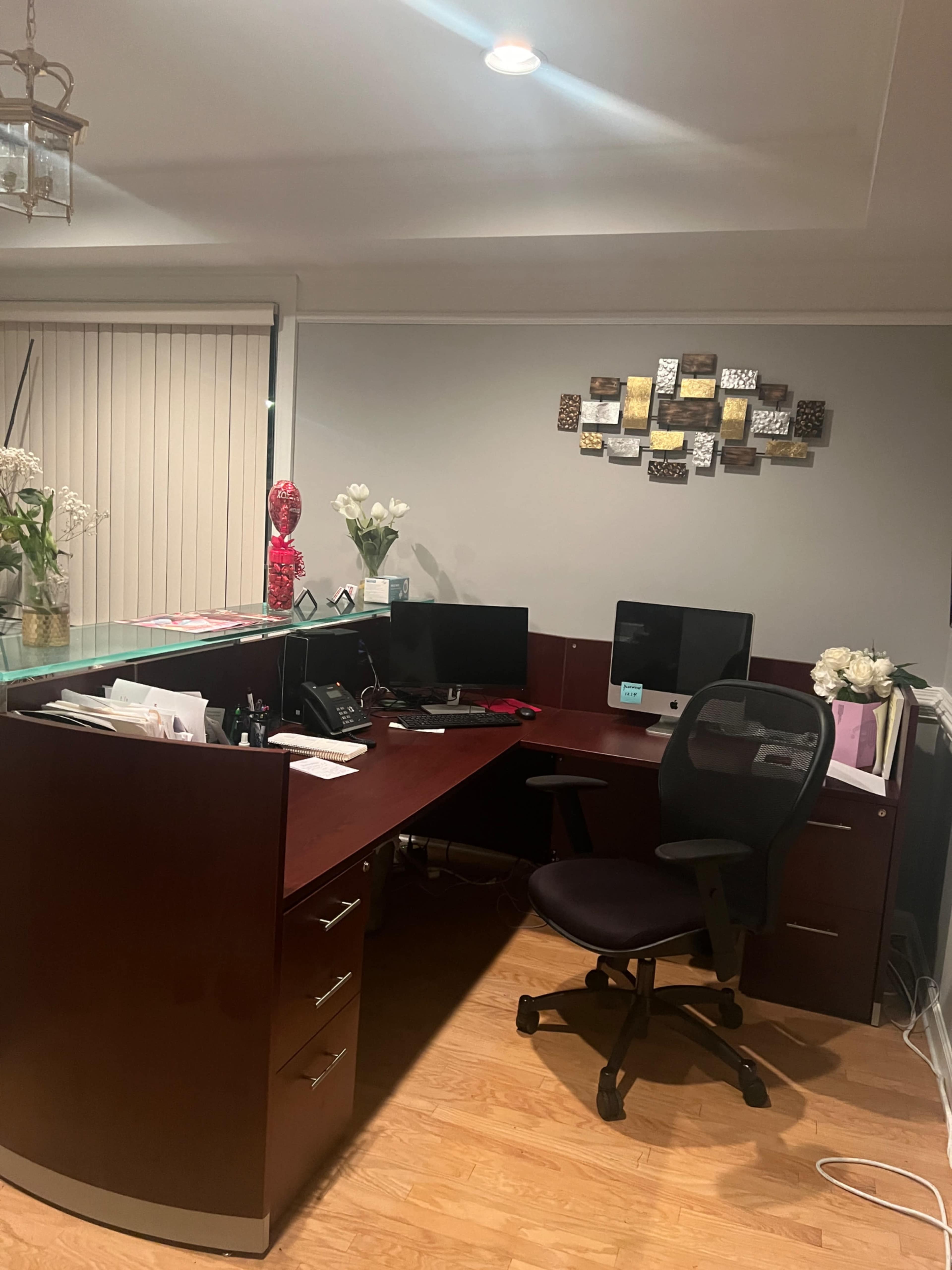 A modern office space features a wooden desk with dual computer monitors, a black ergonomic chair, and decorative items on the wall.