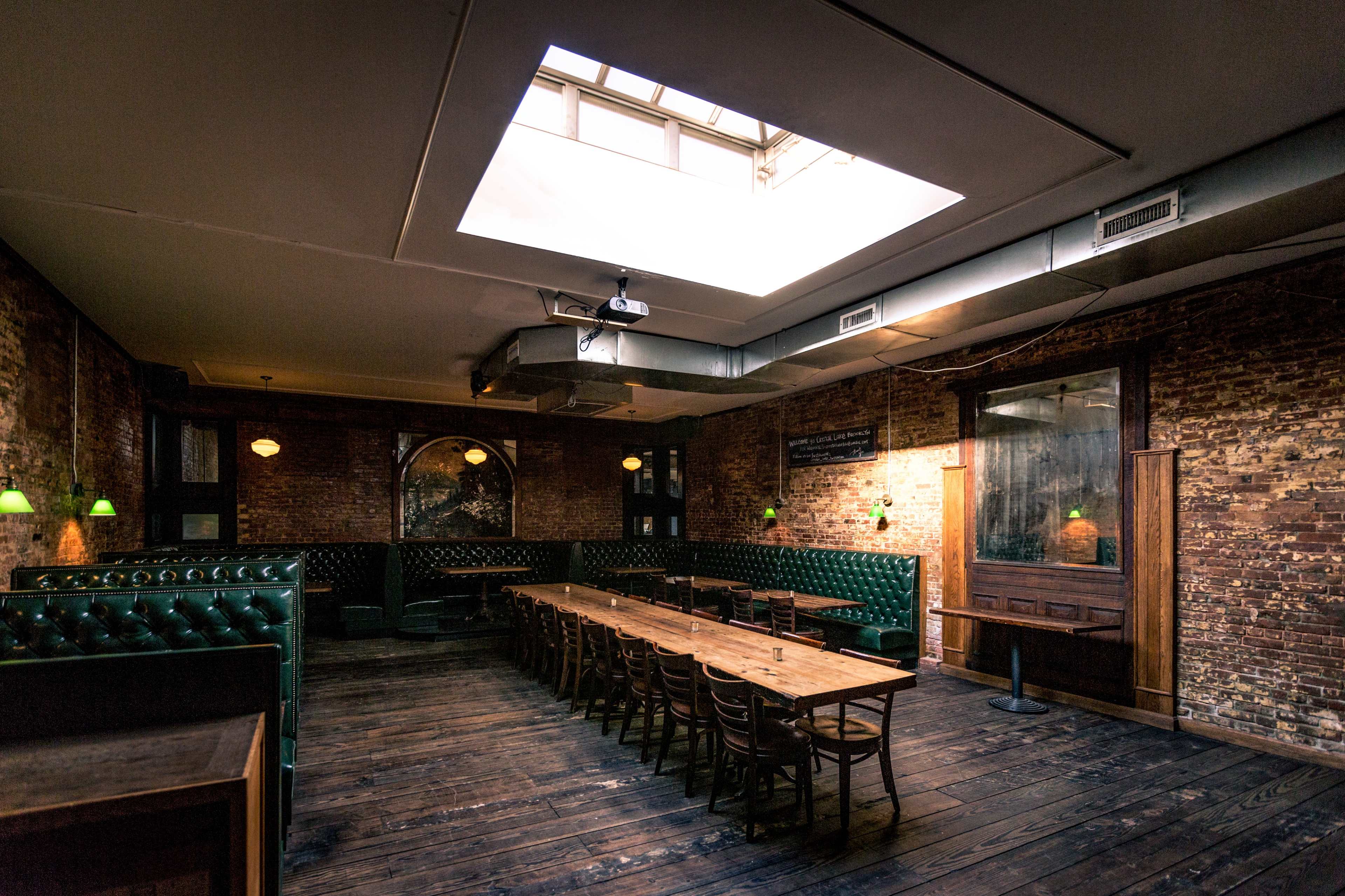 A spacious dining area features a long wooden table surrounded by chairs, with exposed brick walls and a skylight above.