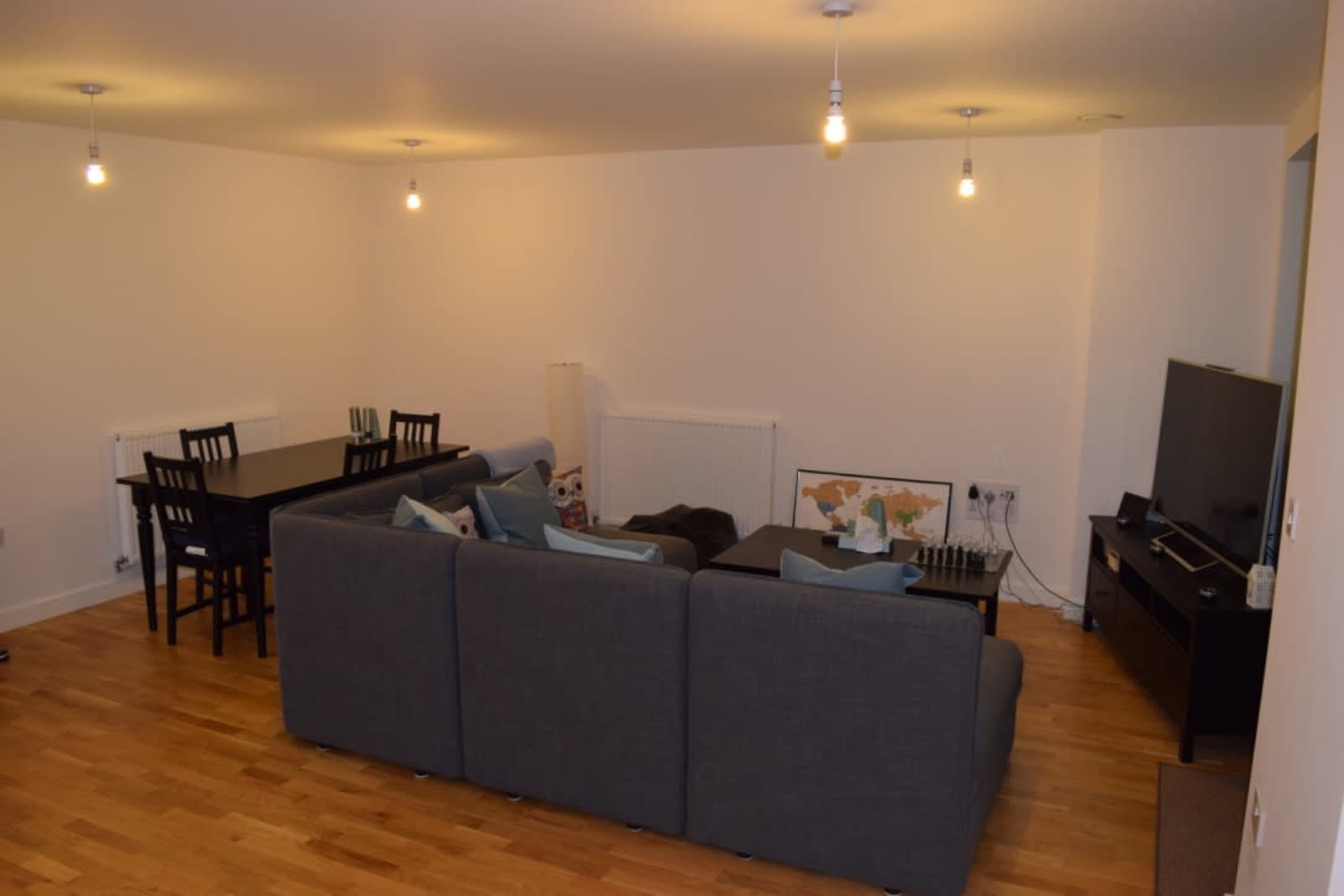 A modern living space with a dark gray sectional sofa, a dining area with a table and chairs, and a television on a low cabinet.