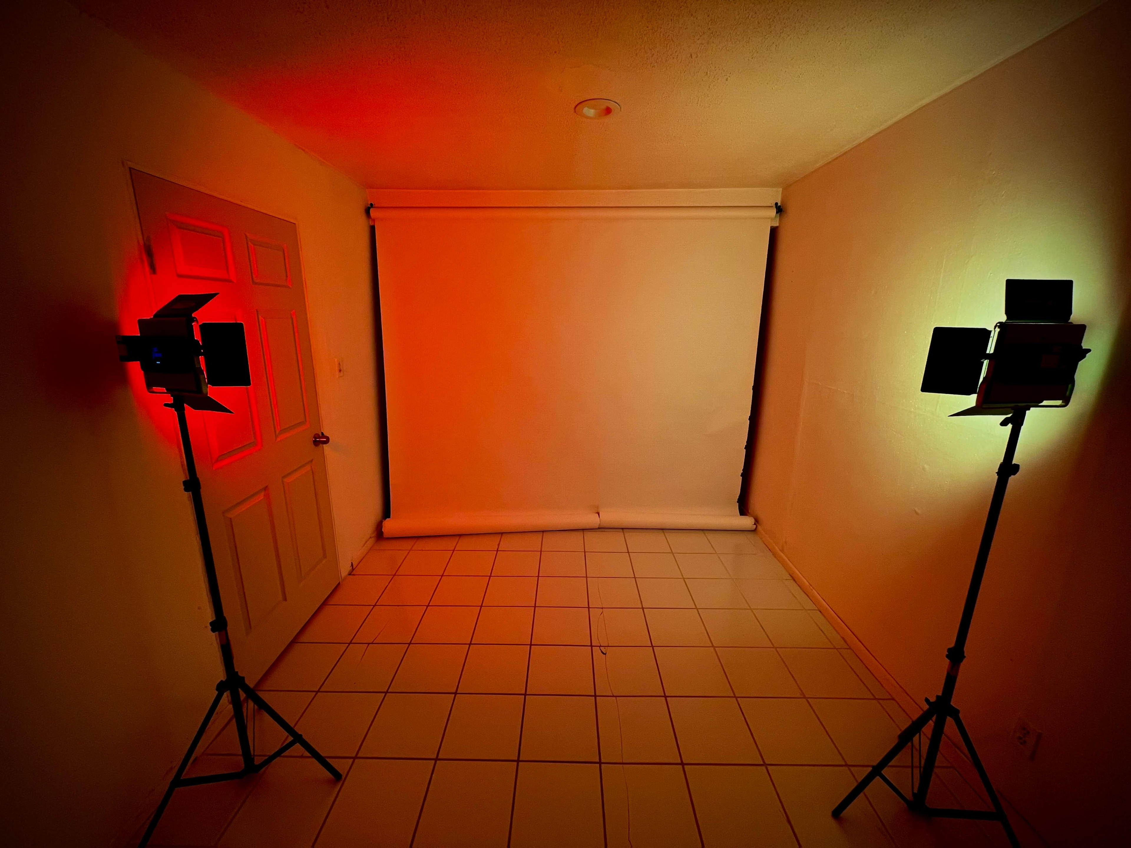 A small room with a blank white backdrop and two studio lights, one red and one green, positioned on either side.