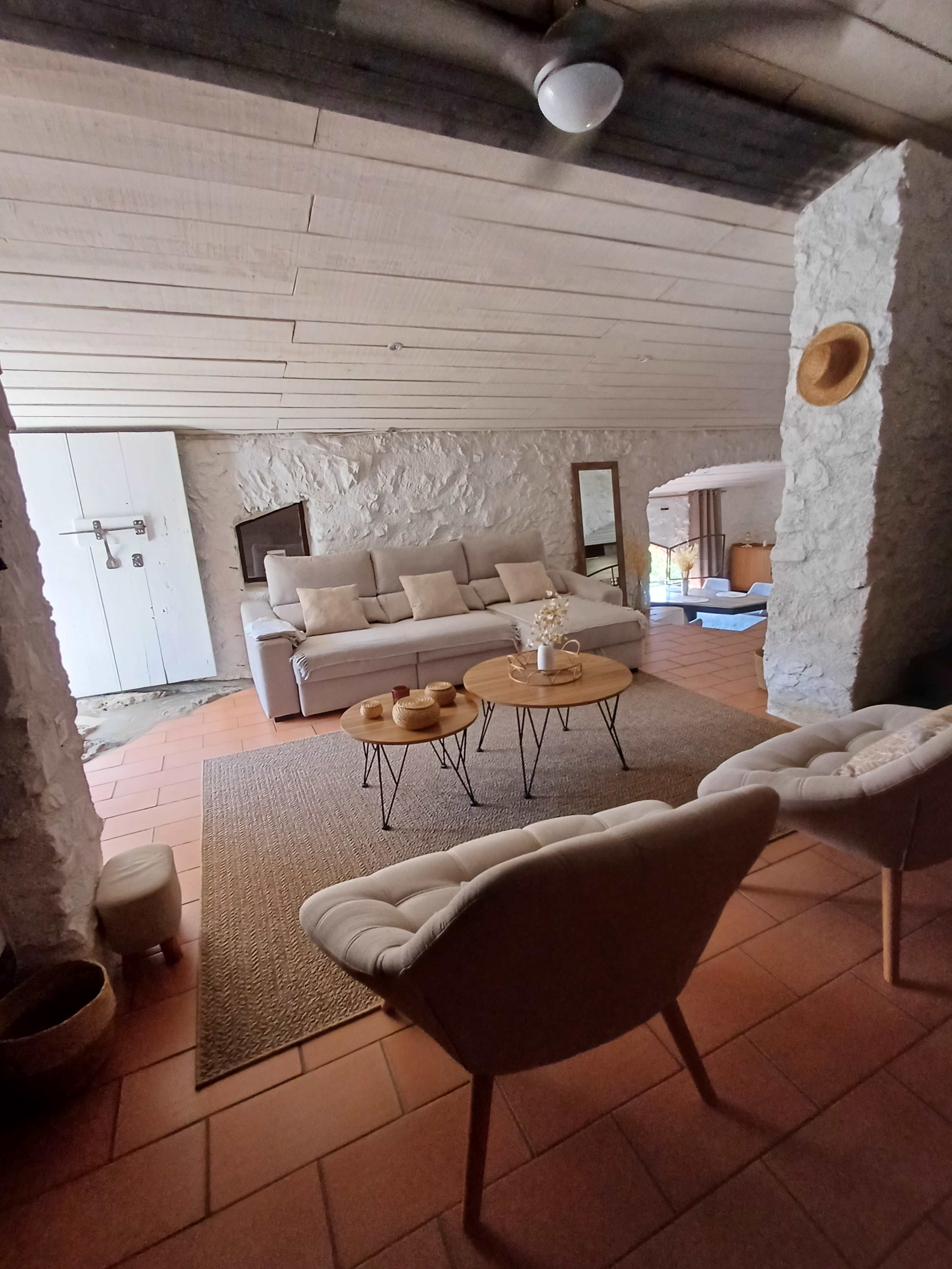 The image shows a living room with stone walls, a sofa, two chairs, a round coffee table, and a woven area rug.