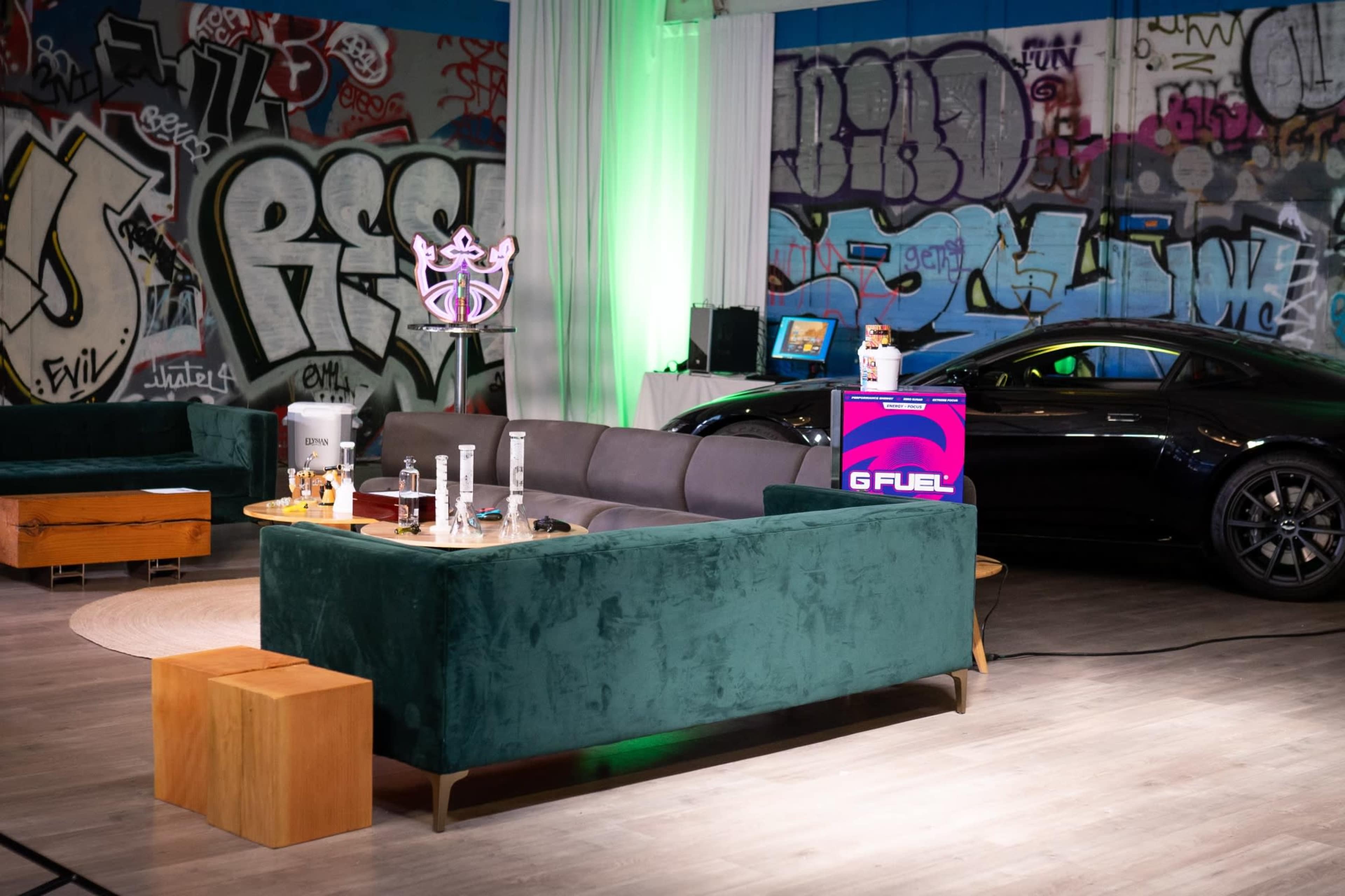 A modern lounge area with a green sofa, wooden tables, and colorful graffiti on the walls, alongside a sports car.