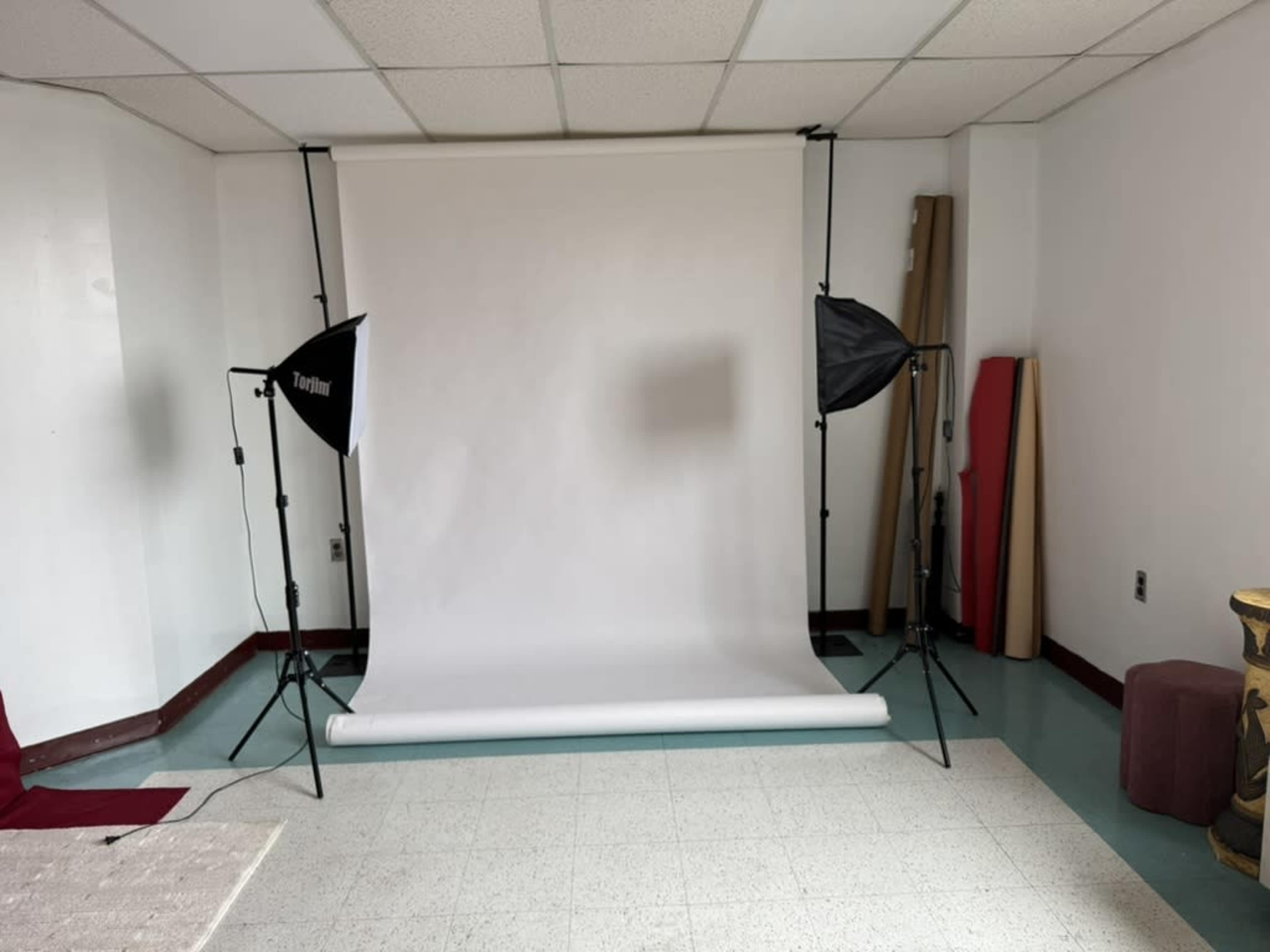 The image shows a photography studio setup with a white backdrop and two softbox lights on either side.