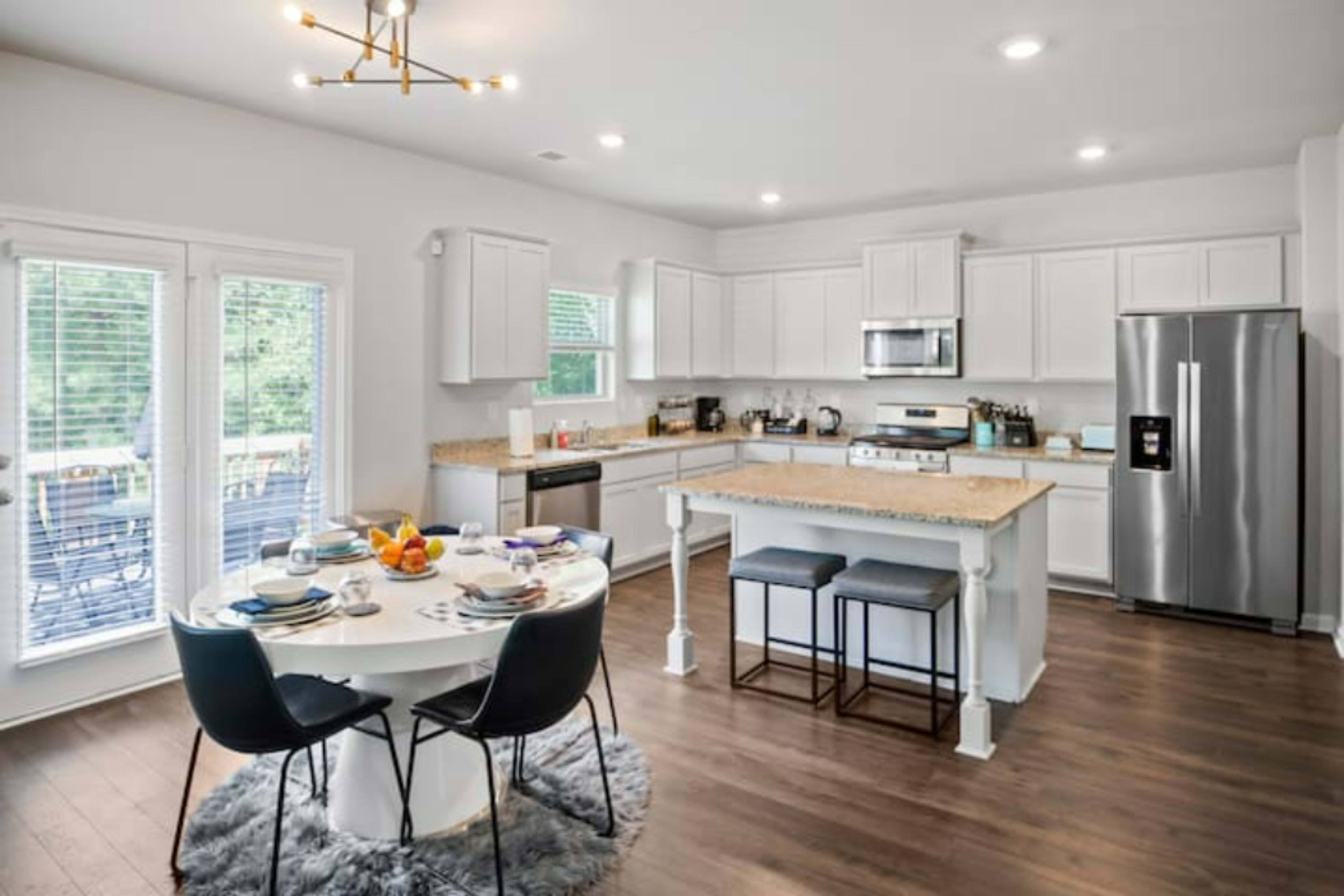 A modern kitchen with a circular dining table set for a meal, featuring a stainless steel refrigerator and white cabinetry.