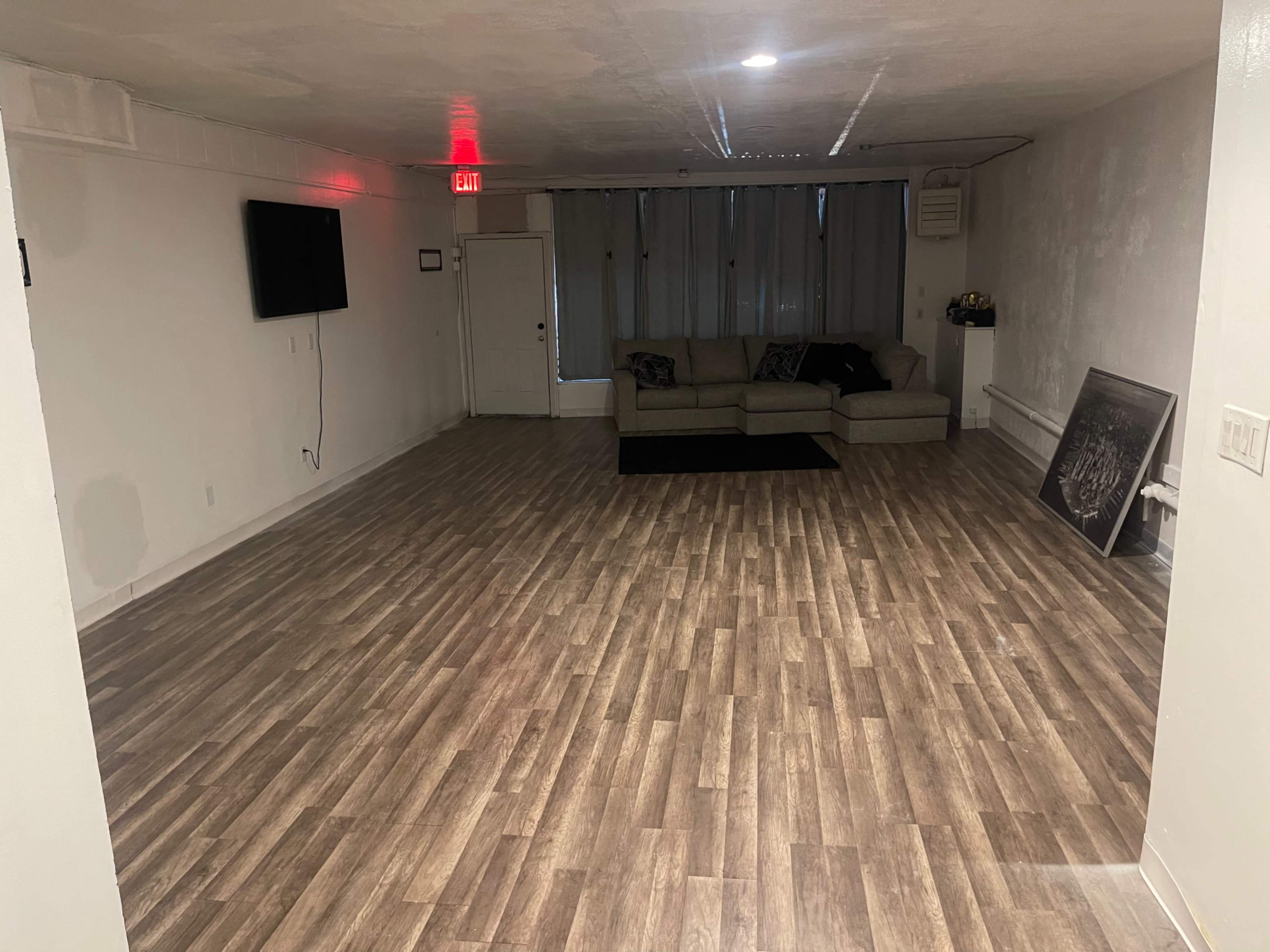 A spacious indoor room with a light-colored floor, a large sofa, and a television mounted on the wall.