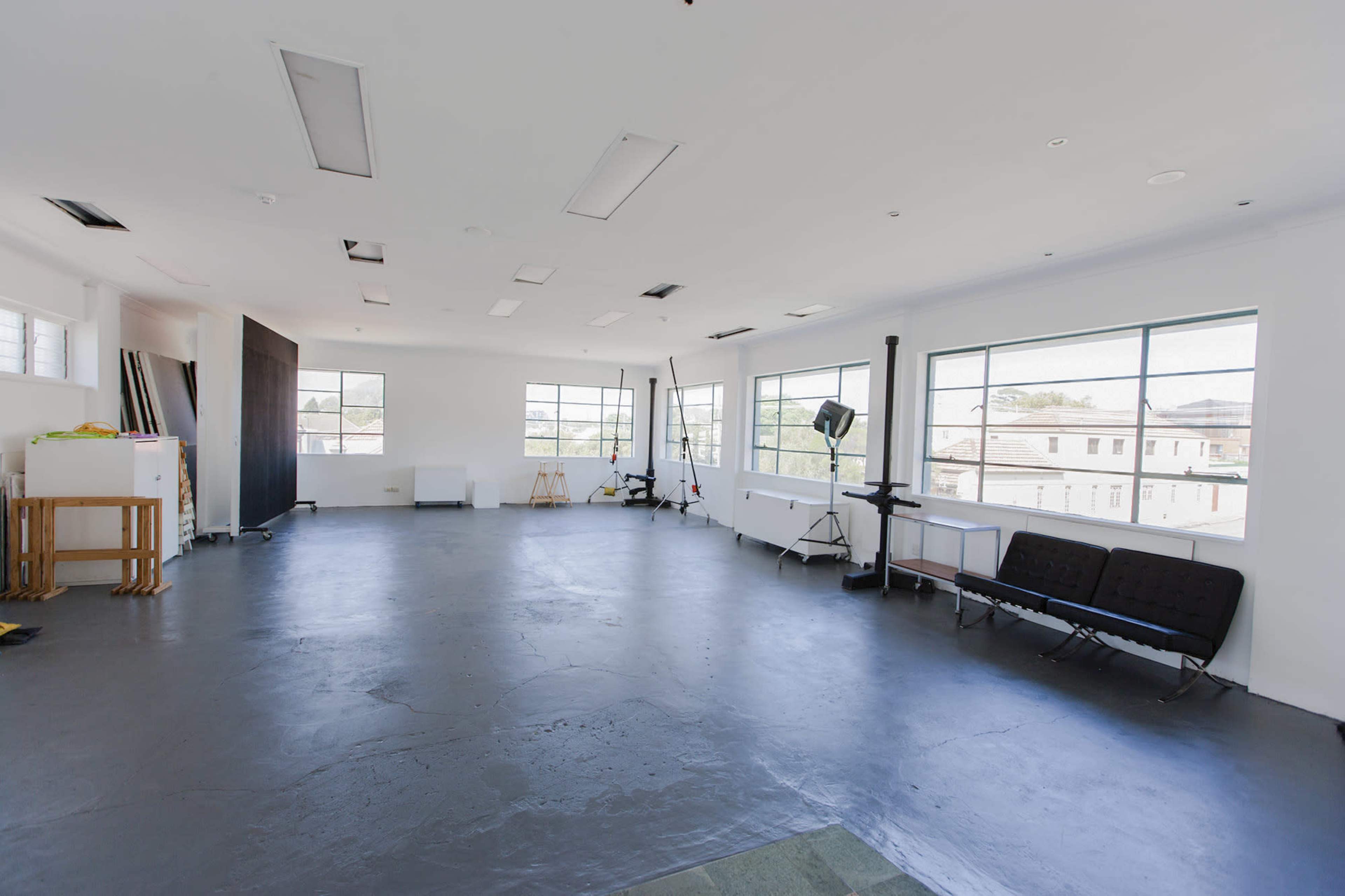 A spacious, empty studio with large windows and minimal furniture arranged along the walls.