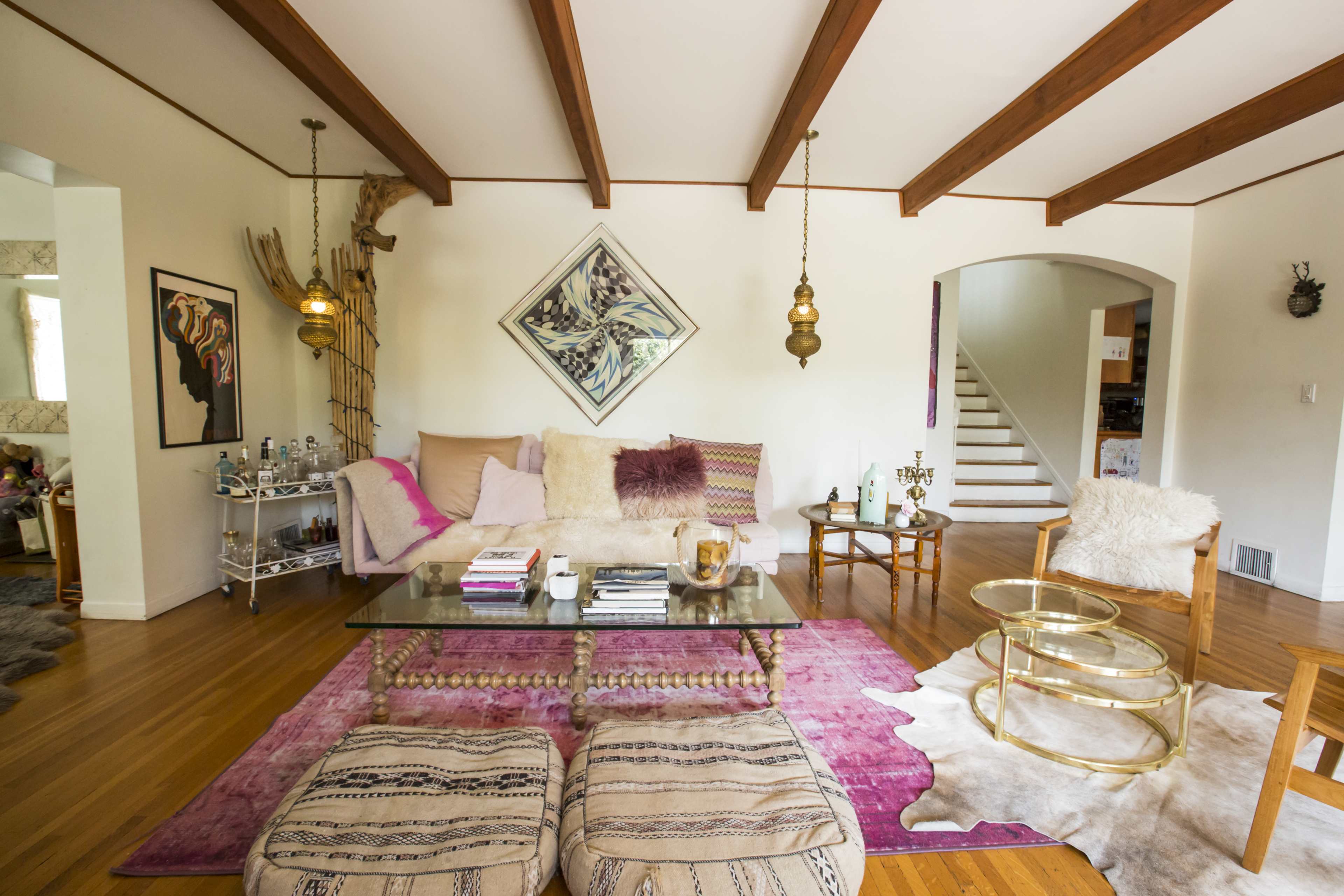 The living room features a cream sofa with purple and pink accents, a glass coffee table on a patterned rug, and wooden beams on the ceiling.