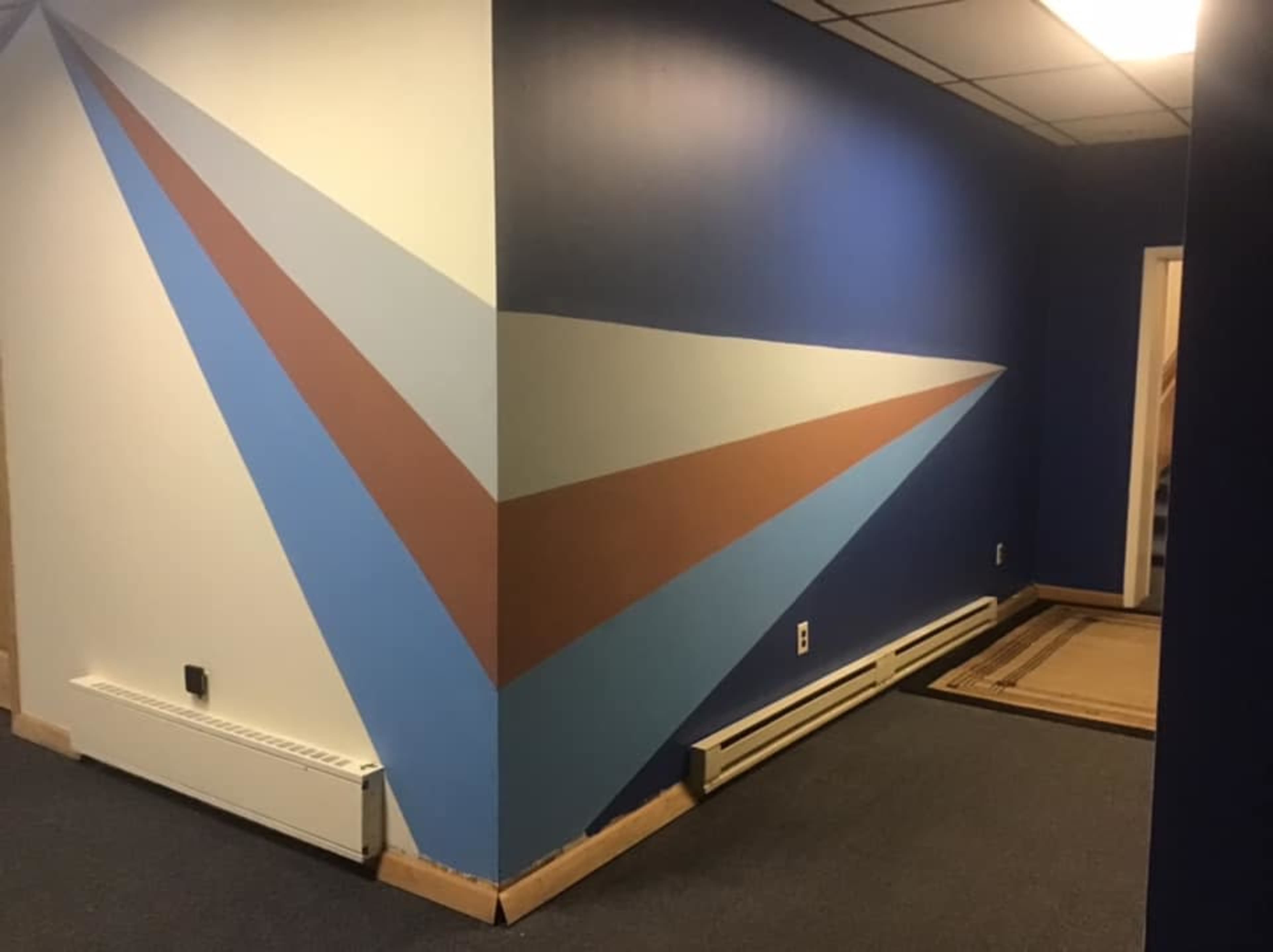 A hallway with a wall featuring a geometric design of blue, brown, and cream stripes leading toward an interior door.