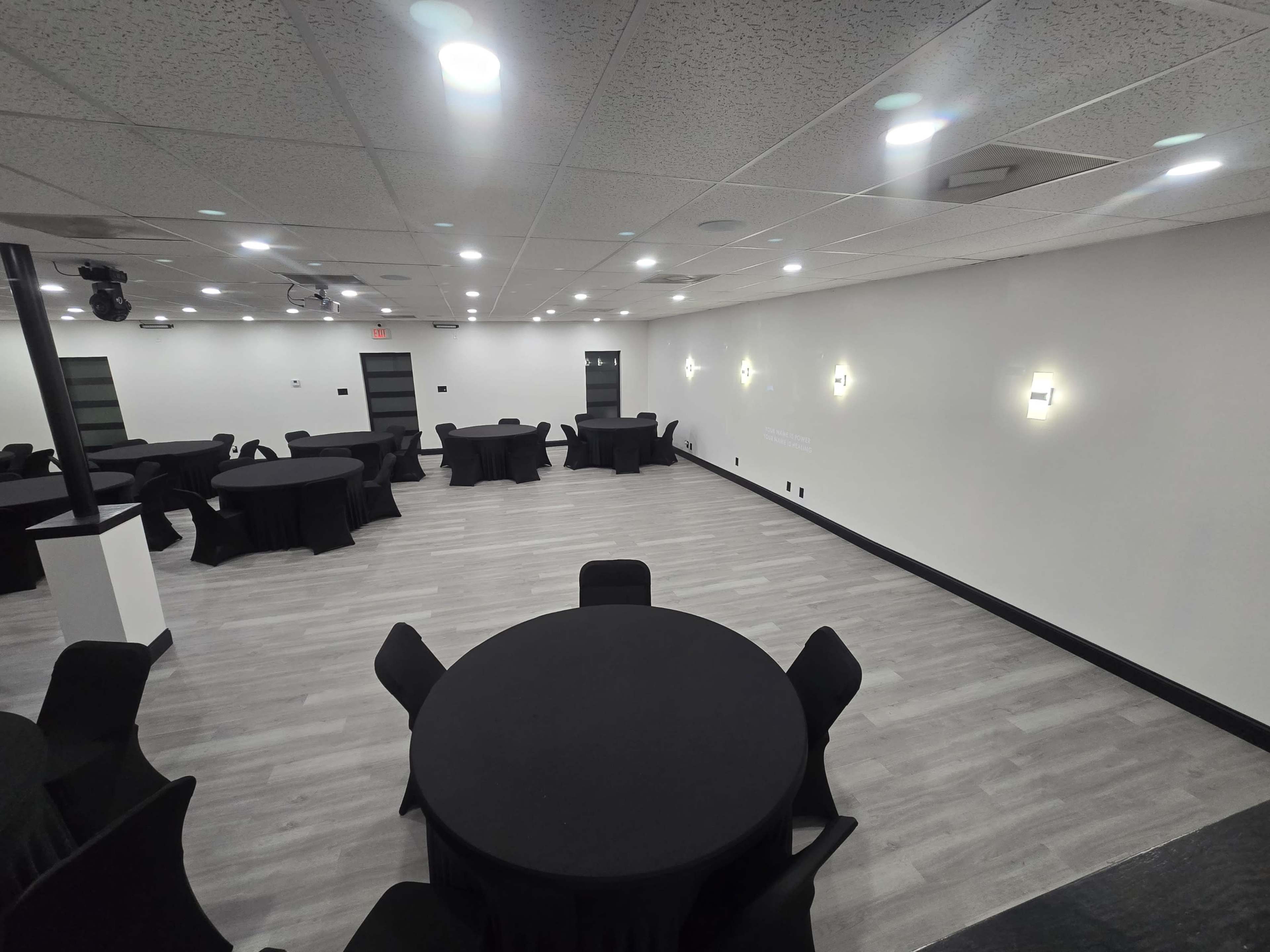 The image shows a large, empty event space with several round tables covered in black tablecloths arranged throughout the room.