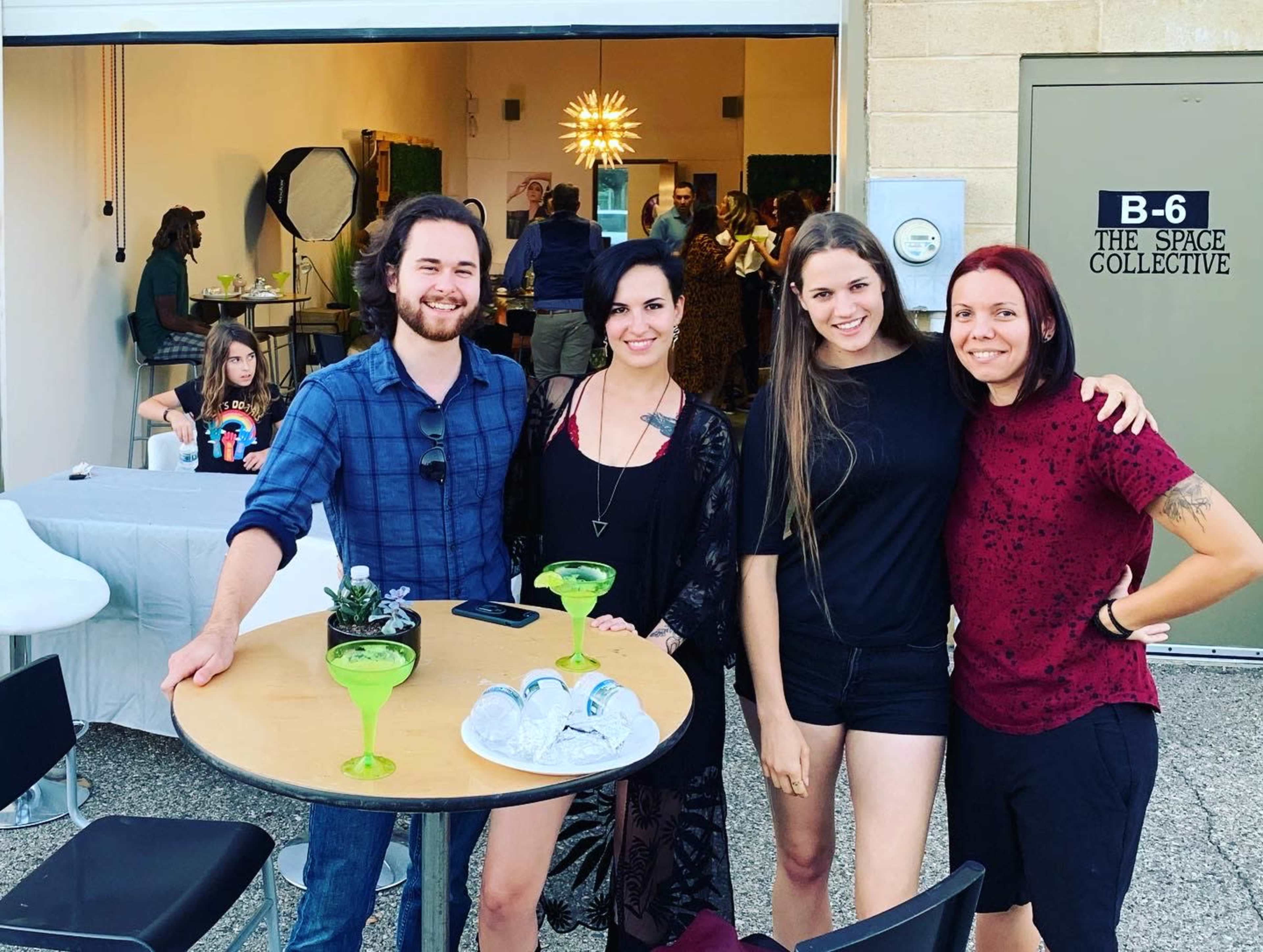 A group of four people poses around a table with drinks outside a building labeled "B-6 THE SPACE COLLECTIVE."
