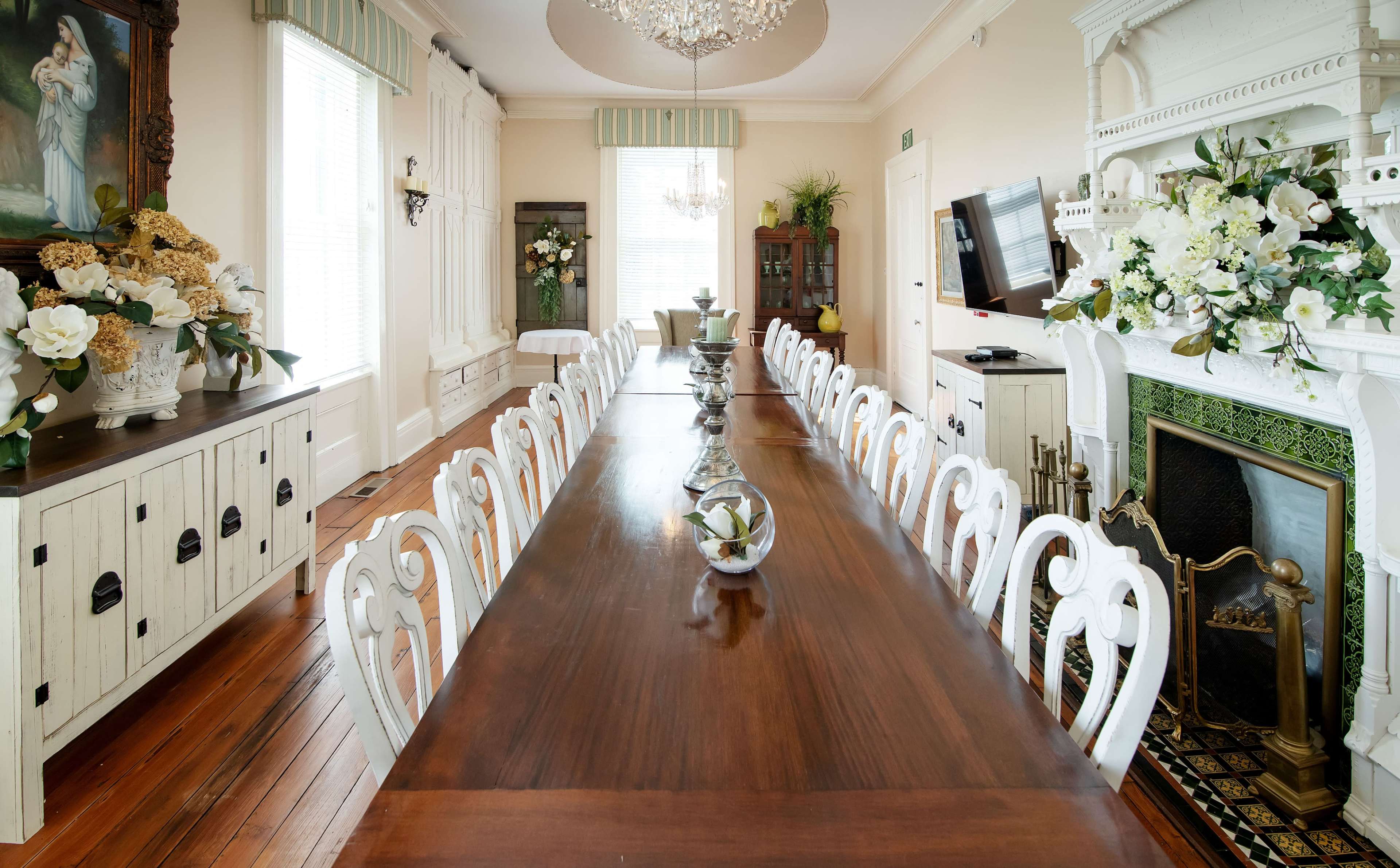 A long wooden dining table set with decorative vases, surrounded by ornate white chairs in a bright, elegantly styled room.